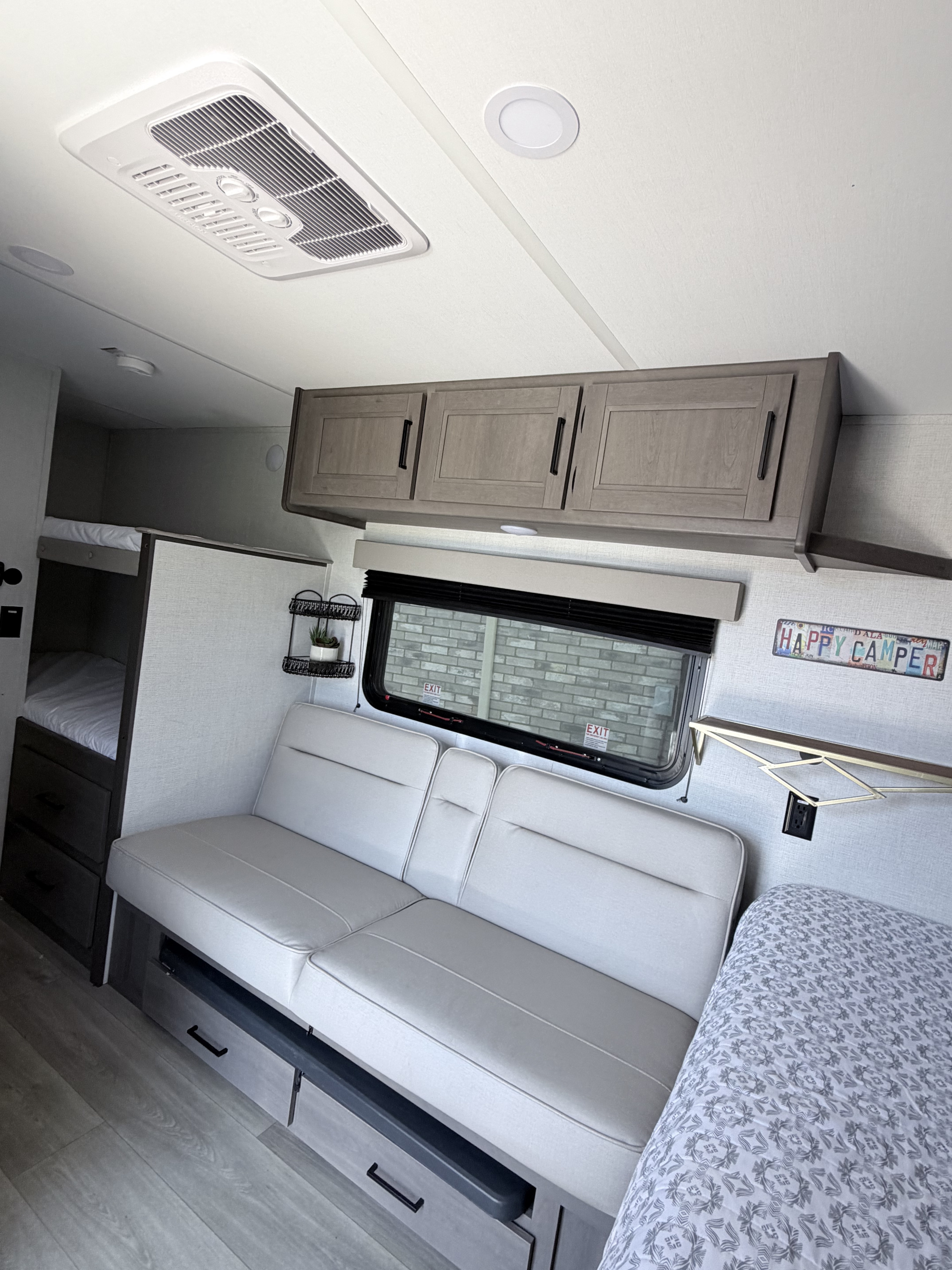 Spacious RV rental interior with light gray bunk beds, couch, overhead cabinets, and AC unit. Perfect for a happy camper trip.. Grand Design Transcend One 2025