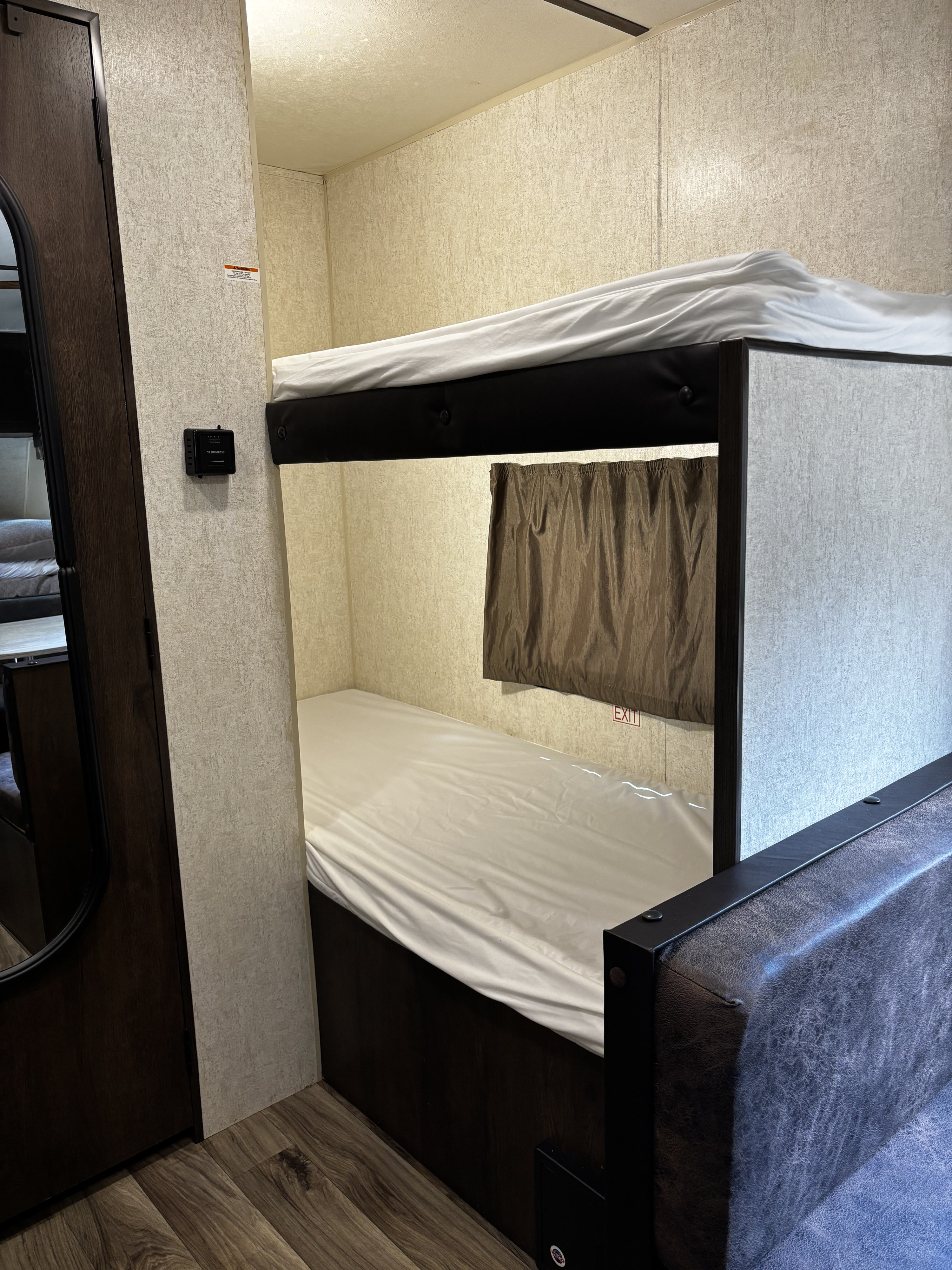 Inside an rv rental, two bunk beds with white sheets, a brown curtain, and a Dometic thermostat on the wall.. Starcraft Autumn Ridge Outfitter 2018