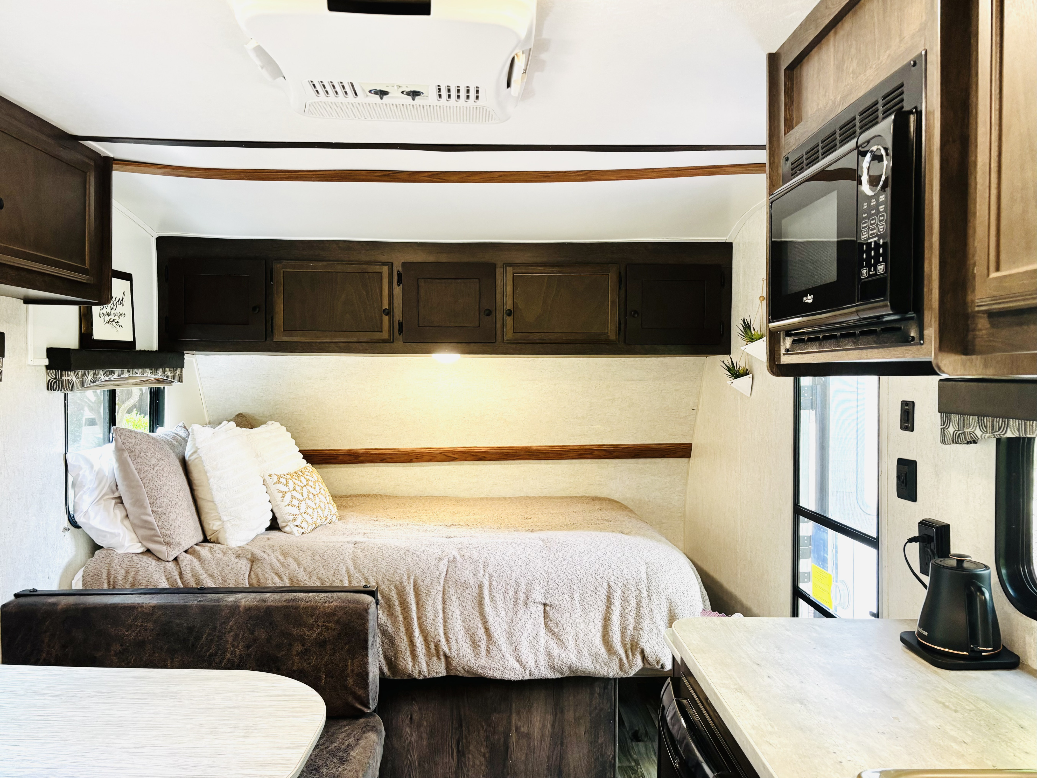 RV rental interior: cozy bedroom with pillows, overhead cabinets, microwave, and a small dining bench.. Starcraft Autumn Ridge Outfitter 2018