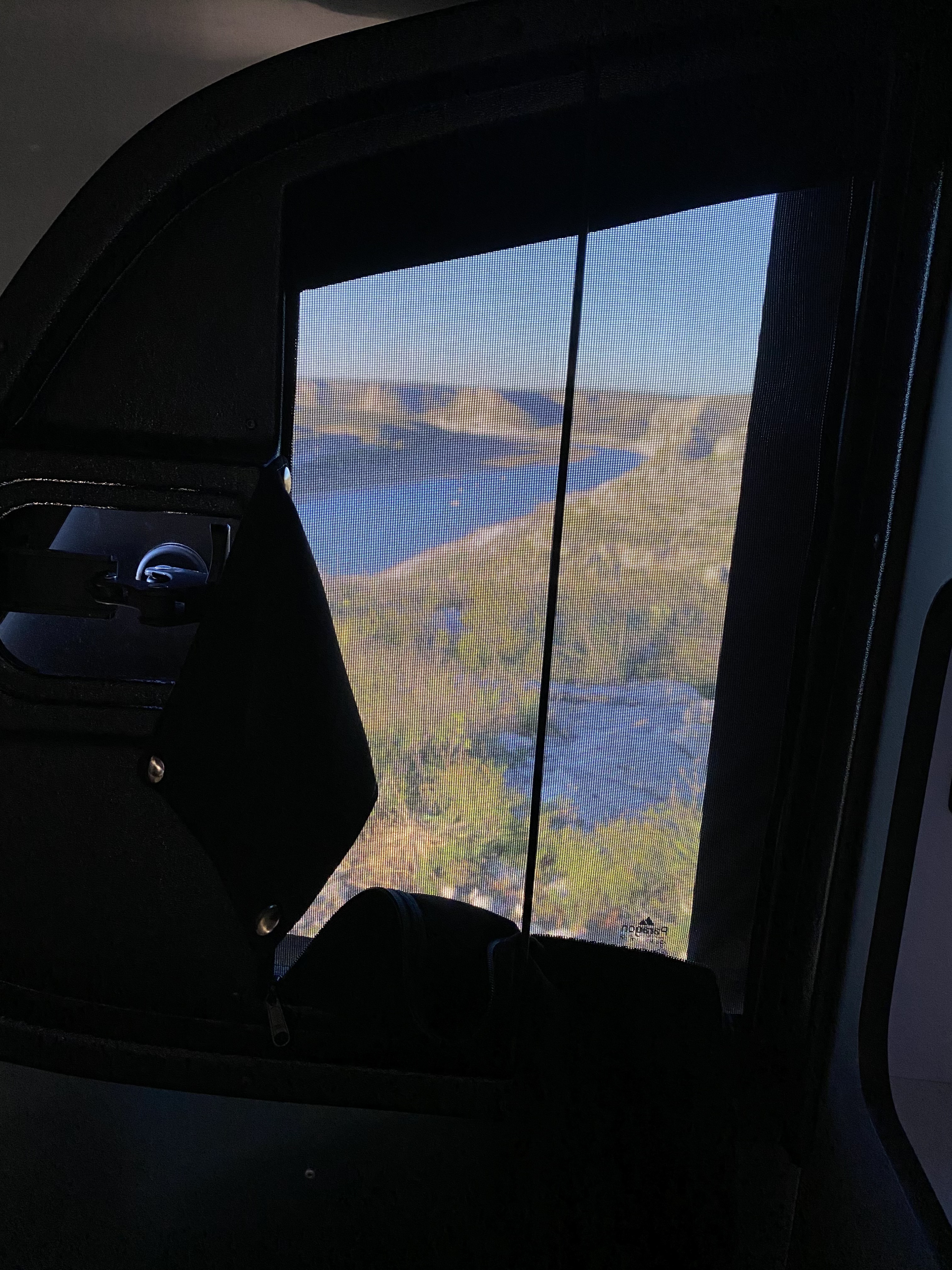 RV rental interior view: scenic lake & mountains through a mesh window screen. Enjoy the journey's serene landscape.. Airstream Basecamp 2024