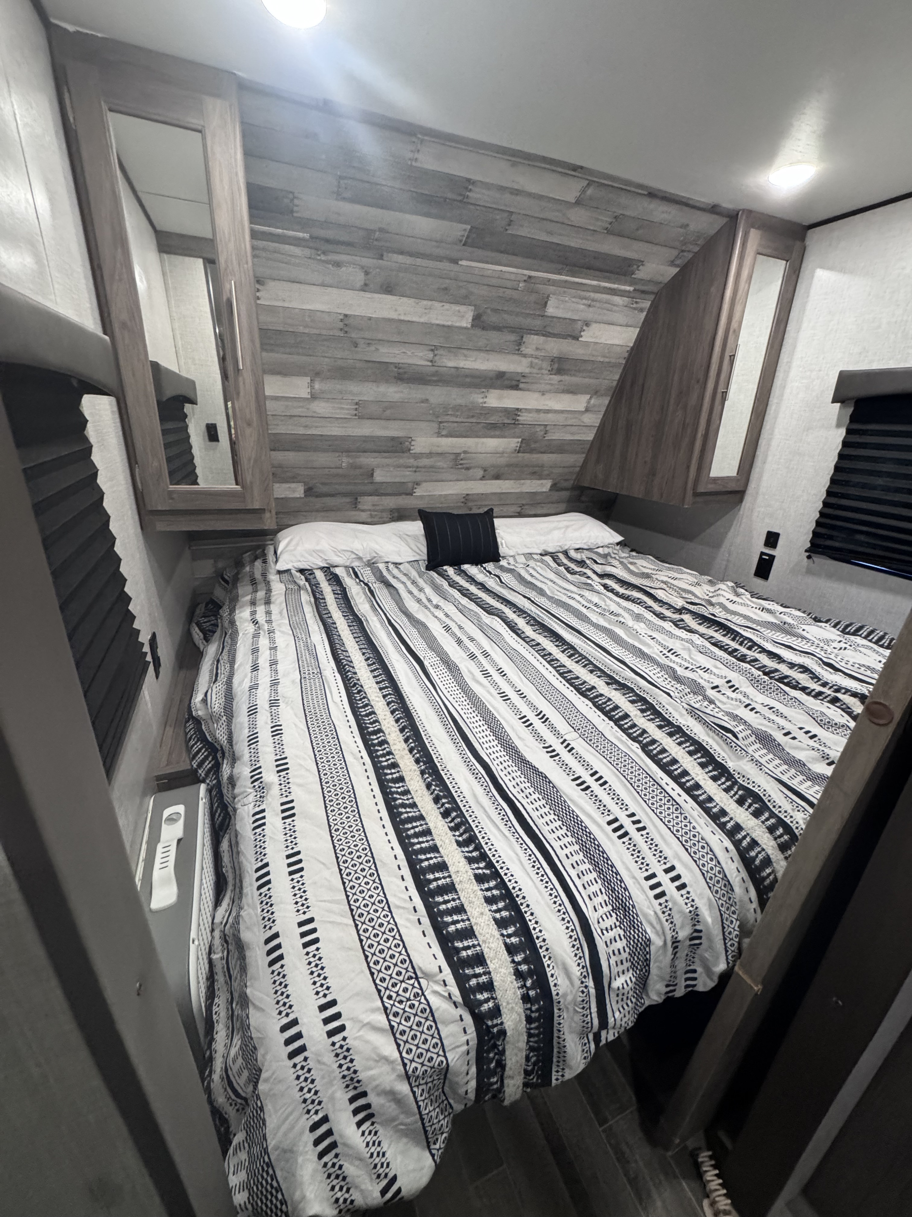 Cozy rv rental bedroom featuring a bed with striped bedding, rustic wood accent wall, and mirrored cabinets. Ideal for comfortable travel.. Crossroads RV Zinger Lite 2022
