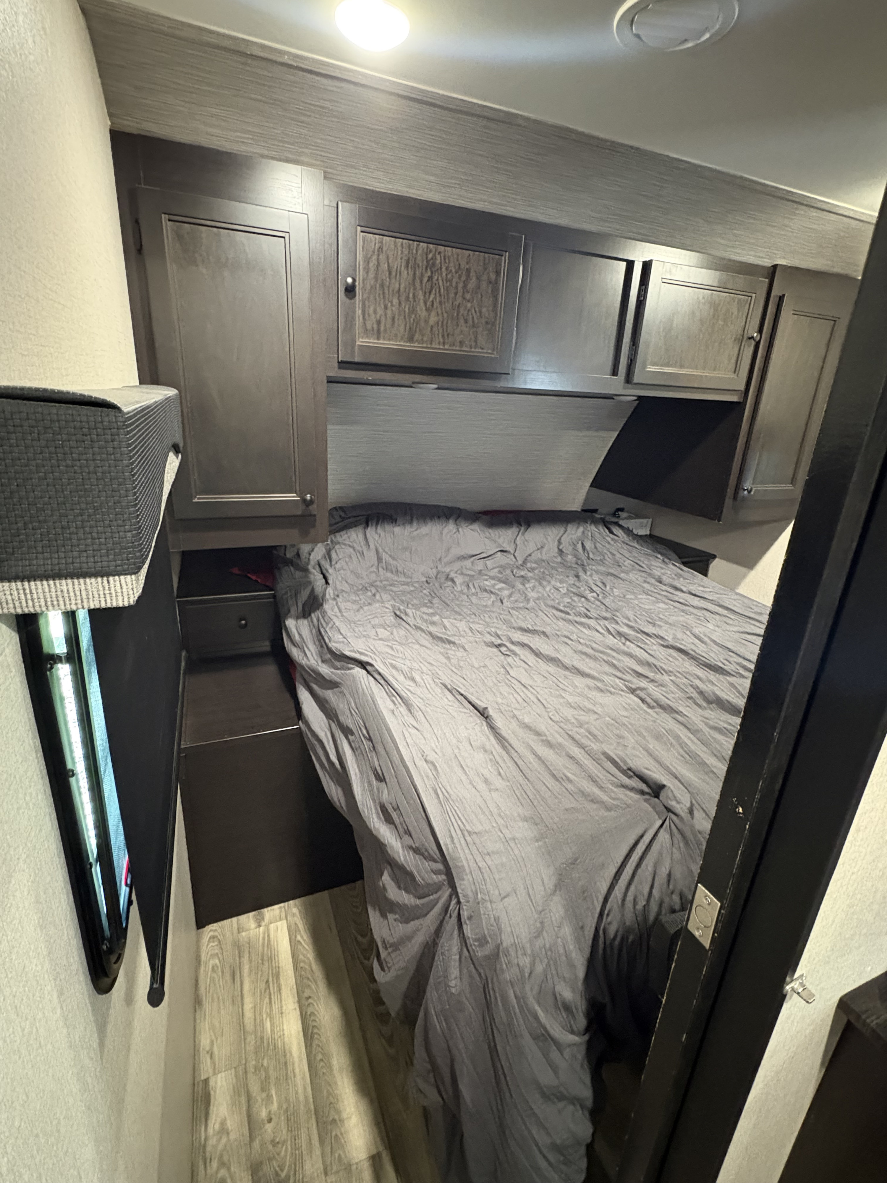 Cozy RV rental bedroom with a grey bed, dark wood cabinets, and overhead storage in a compact space.. Starcraft Super Lite 2022
