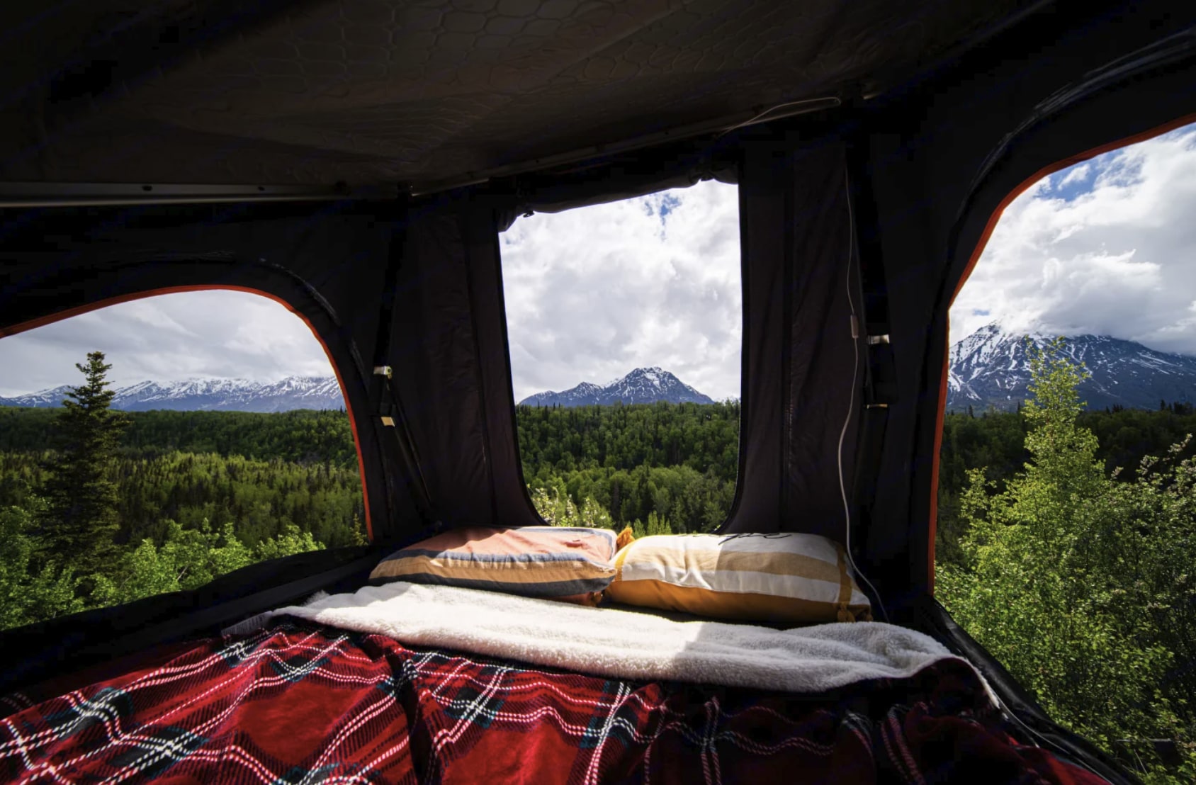 Wake up to nature with this rv rental! Cozy rooftop tent bed shows snowy mountains & lush forests under a cloudy sky.. Ford Explorer 2016