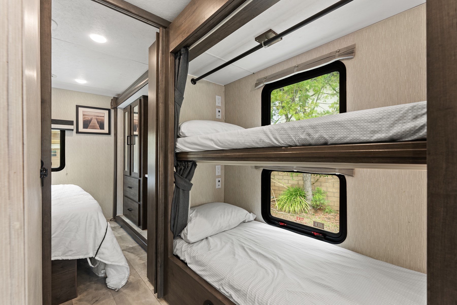 Interior of an RV rental showing modern bunk beds with windows, alongside a glimpse into an adjacent private bedroom with a larger bed.. Coachmen Pursuit 2024