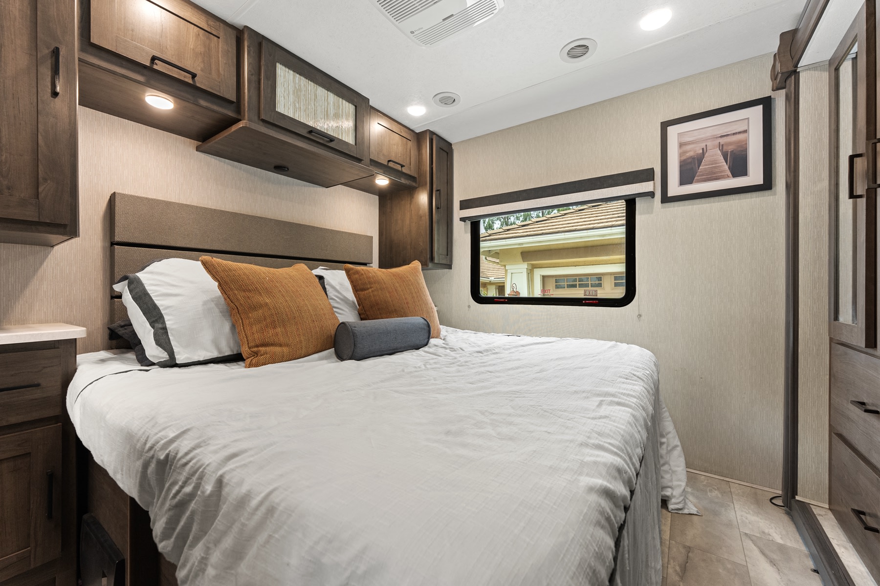 Inviting RV rental bedroom with a comfy bed, overhead cabinets, and a window looking out to a home.. Coachmen Pursuit 2024
