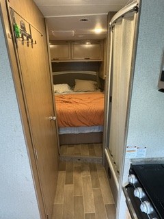 An rv rental interior shows a narrow hallway with a shower on the right, leading to a cozy bedroom with an orange bed.. Thor Chateau 2020