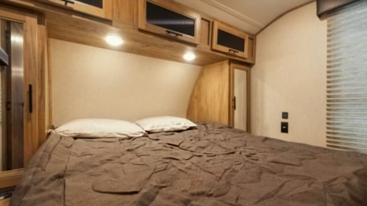 Cozy RV rental bedroom features a comfy bed, wood overhead cabinets with lights, and a window with blinds.. Forest River Alpha Wolf 2021
