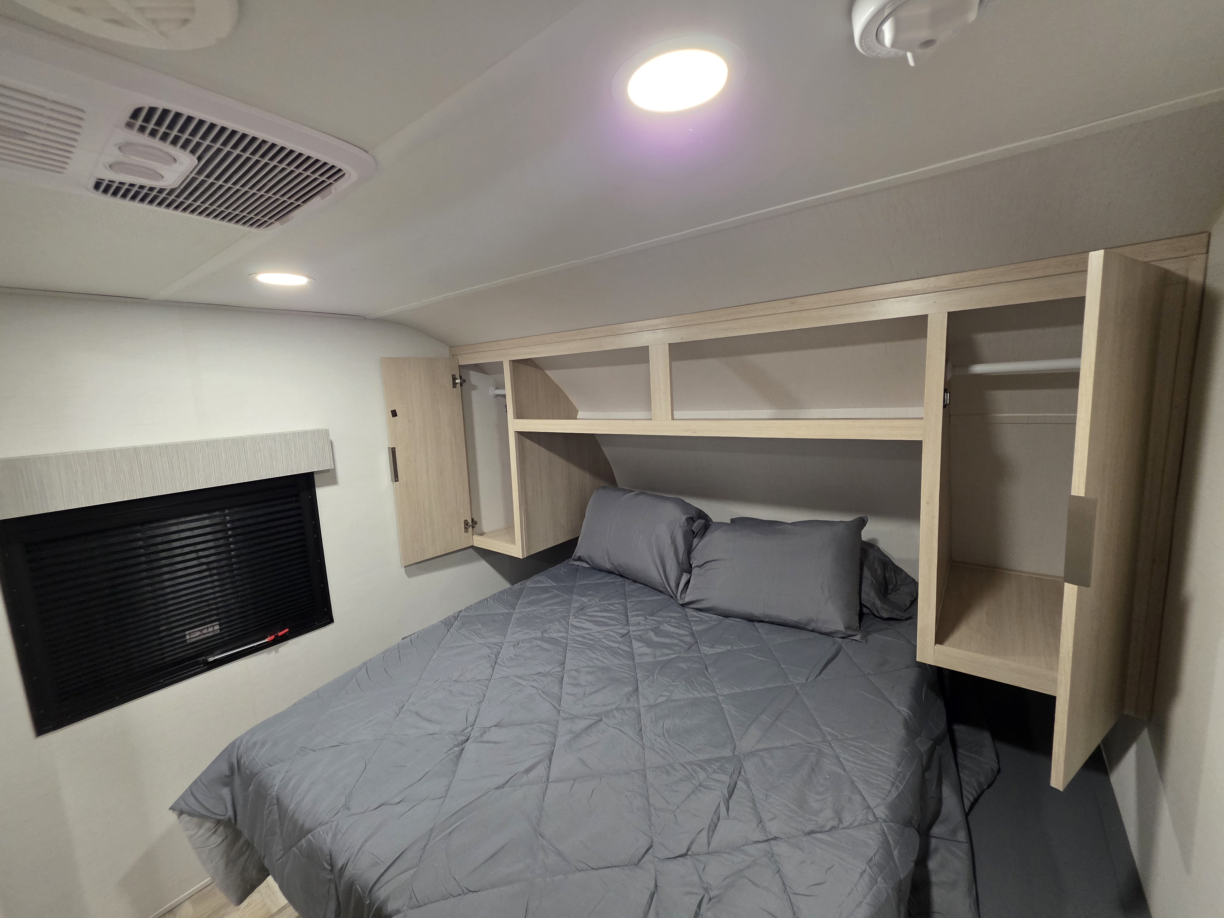 RV rental bedroom with a grey comforter, open overhead storage cabinets, and a ceiling-mounted AC unit.. Forest River Tracer Ultra Lite 2025