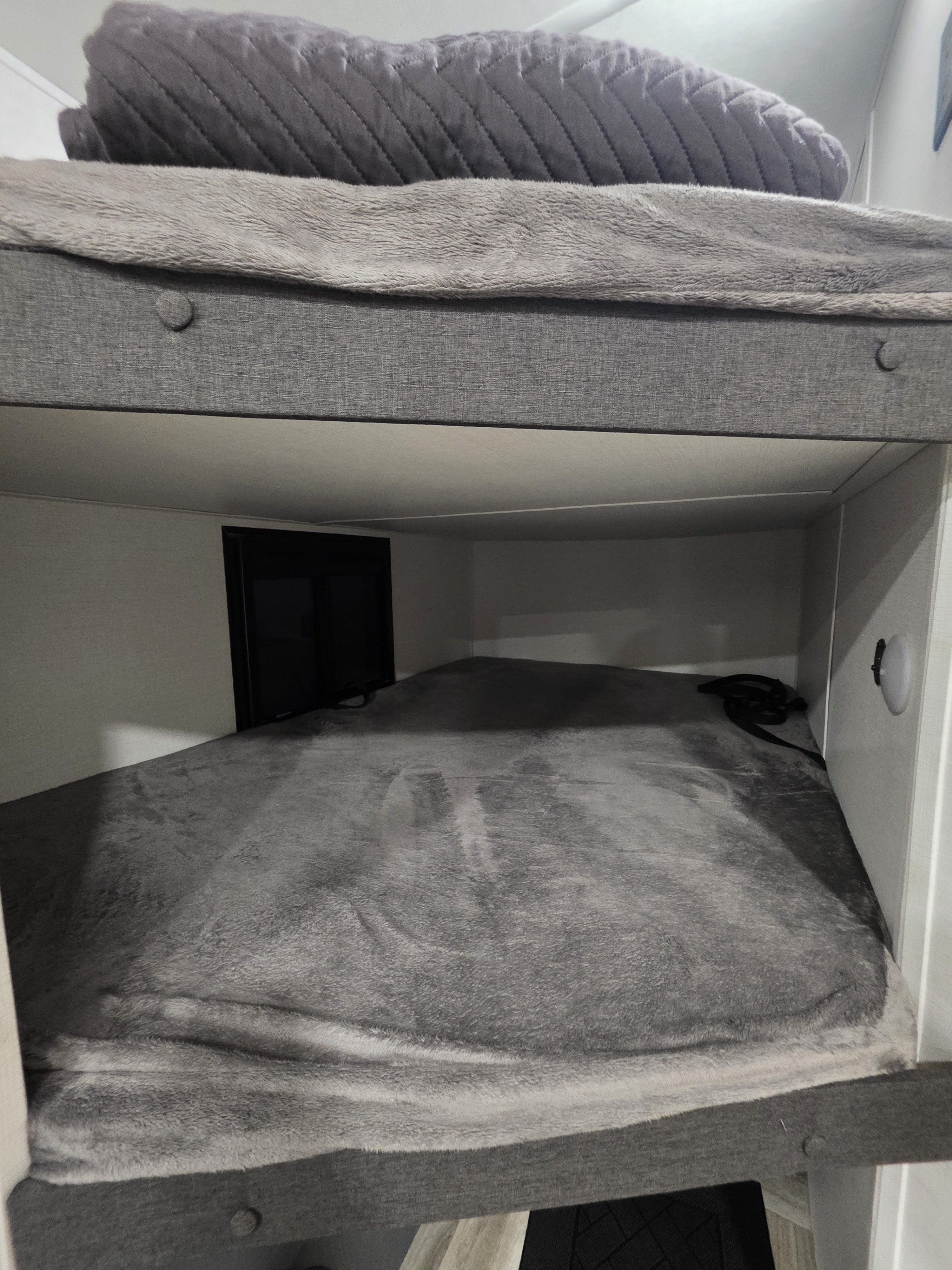 RV rental interior featuring a gray bunk bed setup. The bottom bunk has soft bedding, with a light and strap nearby.. Forest River Tracer Ultra Lite 2025