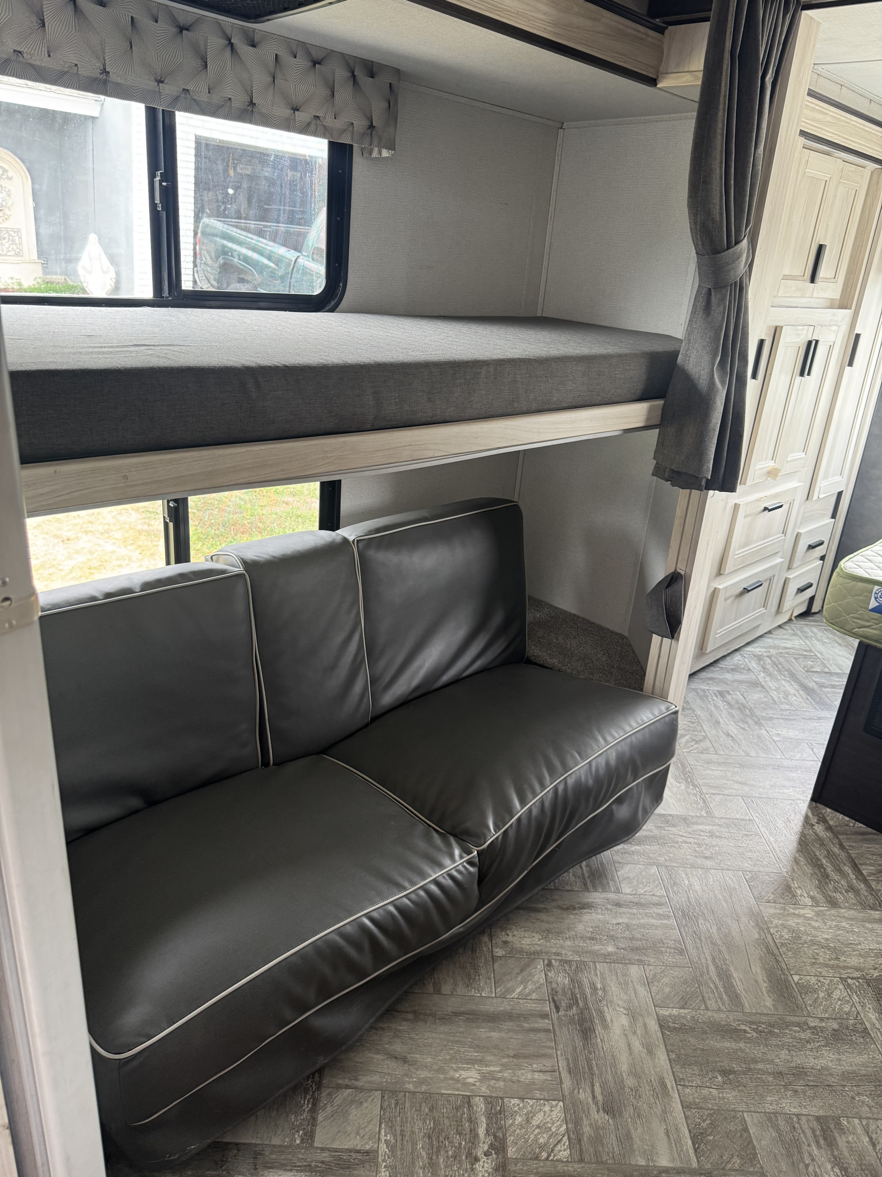 RV rental interior: bunk bed with gray mattress over a dark sofa, light cabinetry & herringbone floor.. Forest River Sunseeker LE 2023