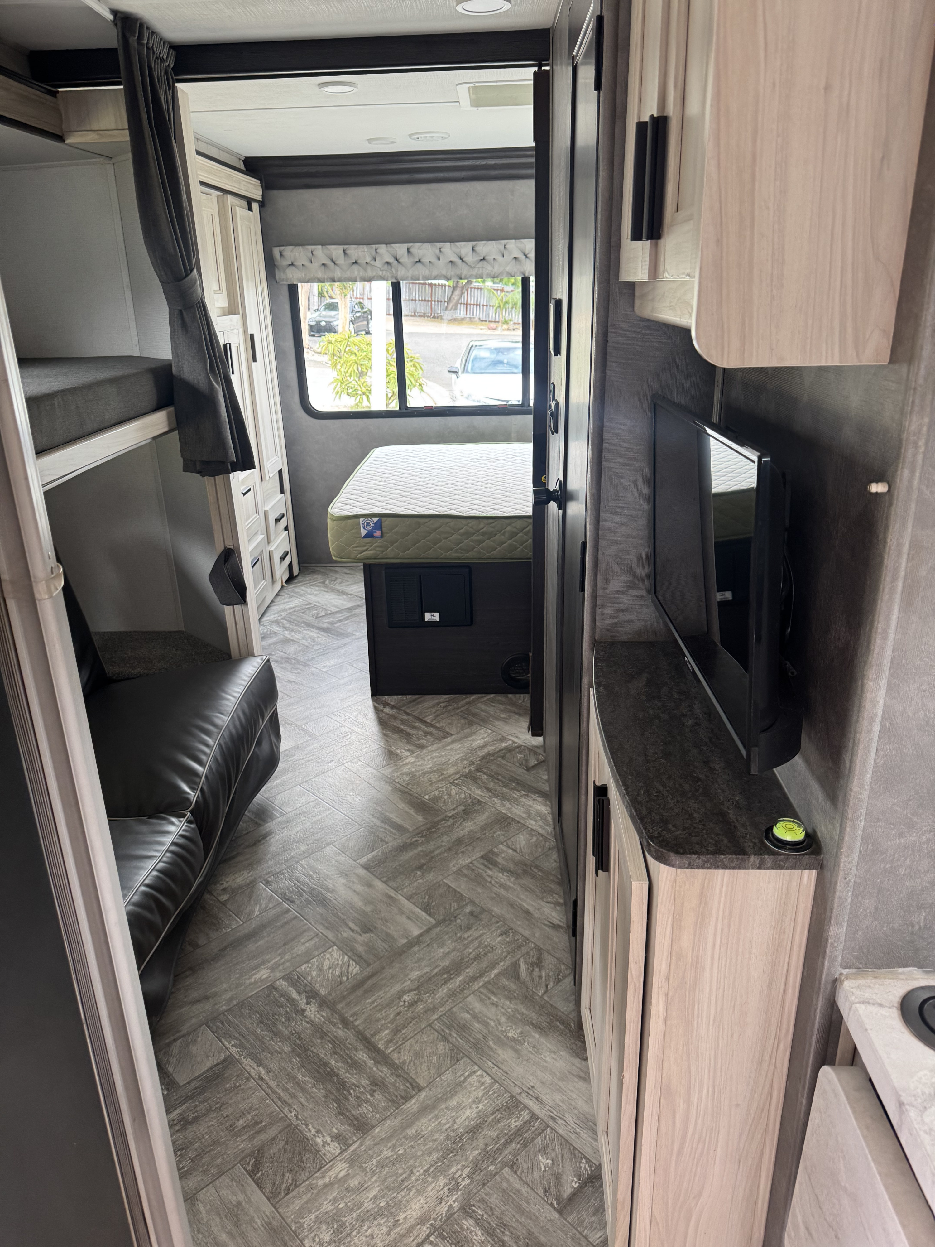 This RV rental interior features bunk beds, a main bed, sofa, TV, and stylish grey herringbone flooring, creating a cozy space.. Forest River Sunseeker LE 2023