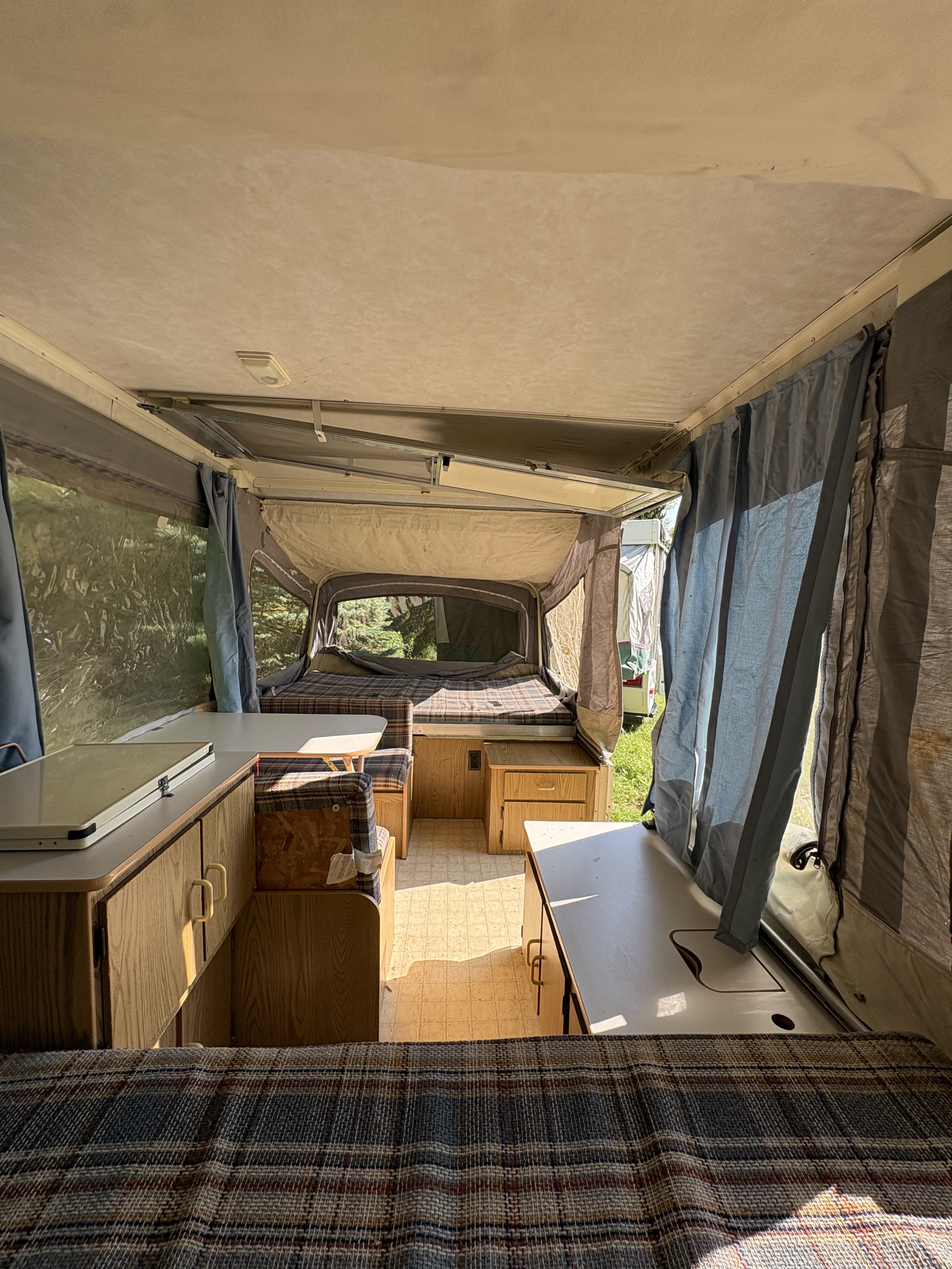 View inside a cozy pop-up camper with plaid beds, dining area, and cabinetry. Ideal for your next RV rental adventure.. Coleman Destiny Roanoke 1991