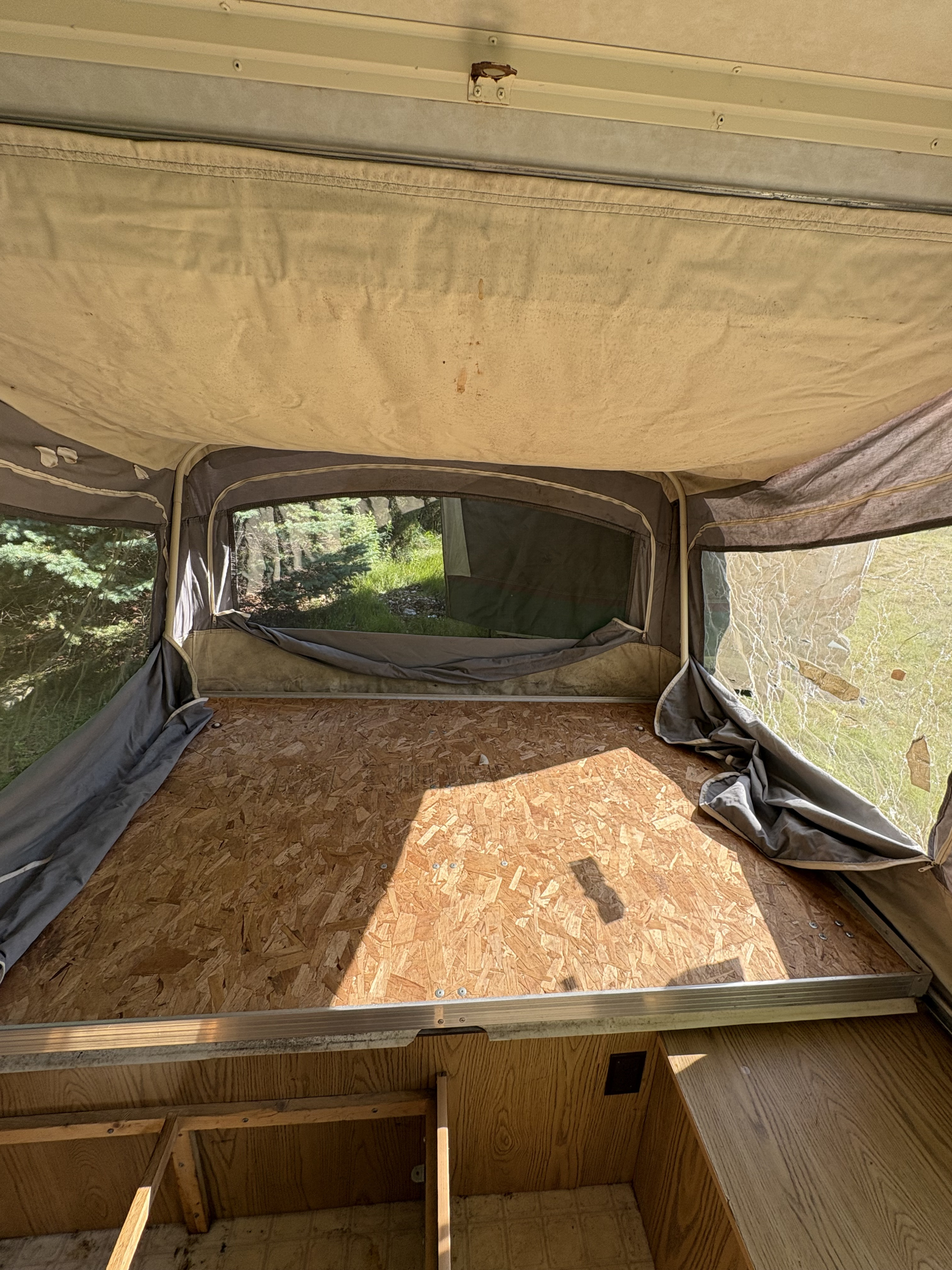 RV rental pop-up camper interior with canvas walls, wooden bed platform, and windows showing forest views.. Coleman Destiny Roanoke 1991