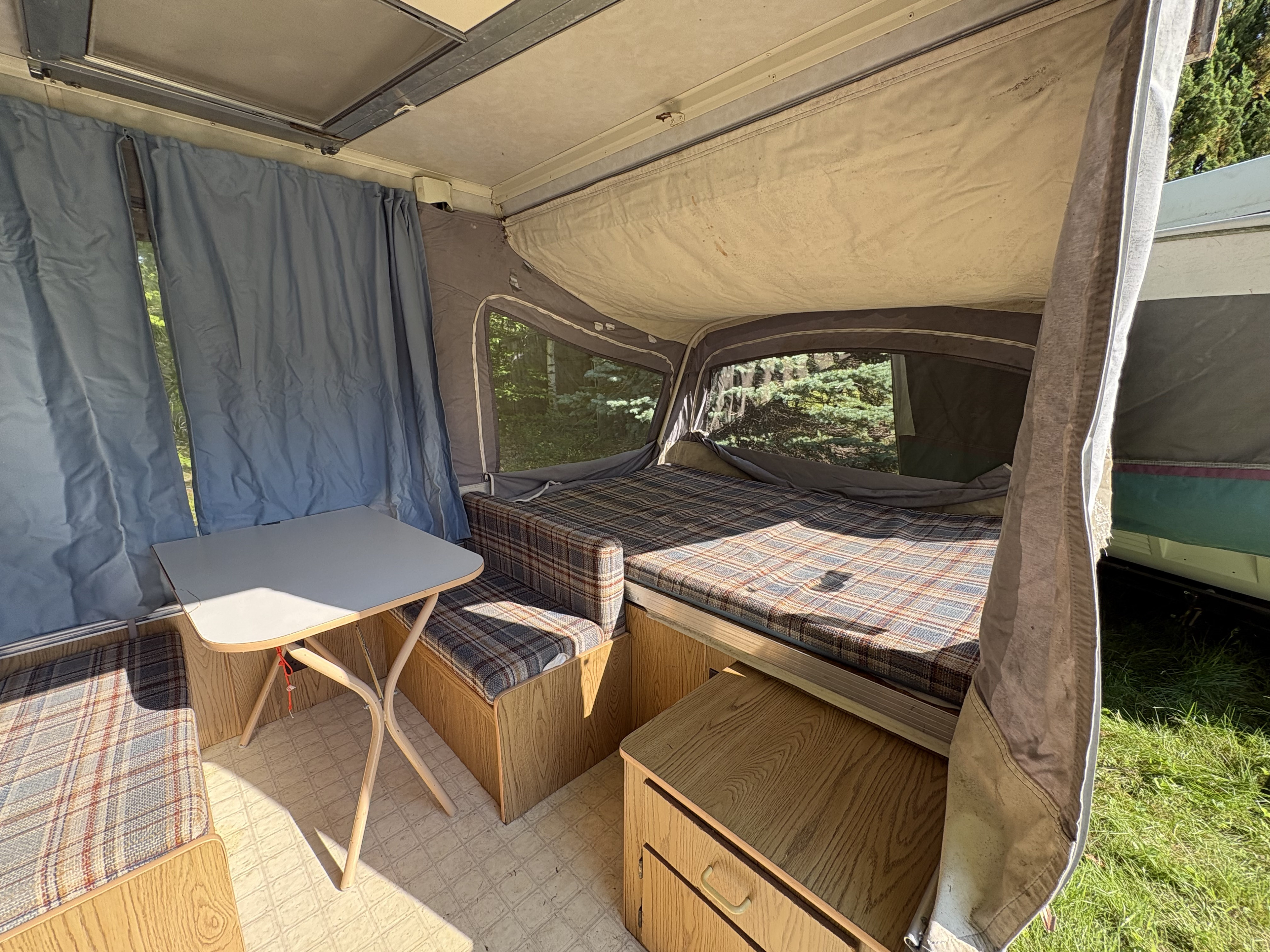 Cozy vintage pop-up camper interior, featuring a plaid bed, dinette, and blue curtains. Perfect for your next RV rental adventure.. Coleman Destiny Roanoke 1991