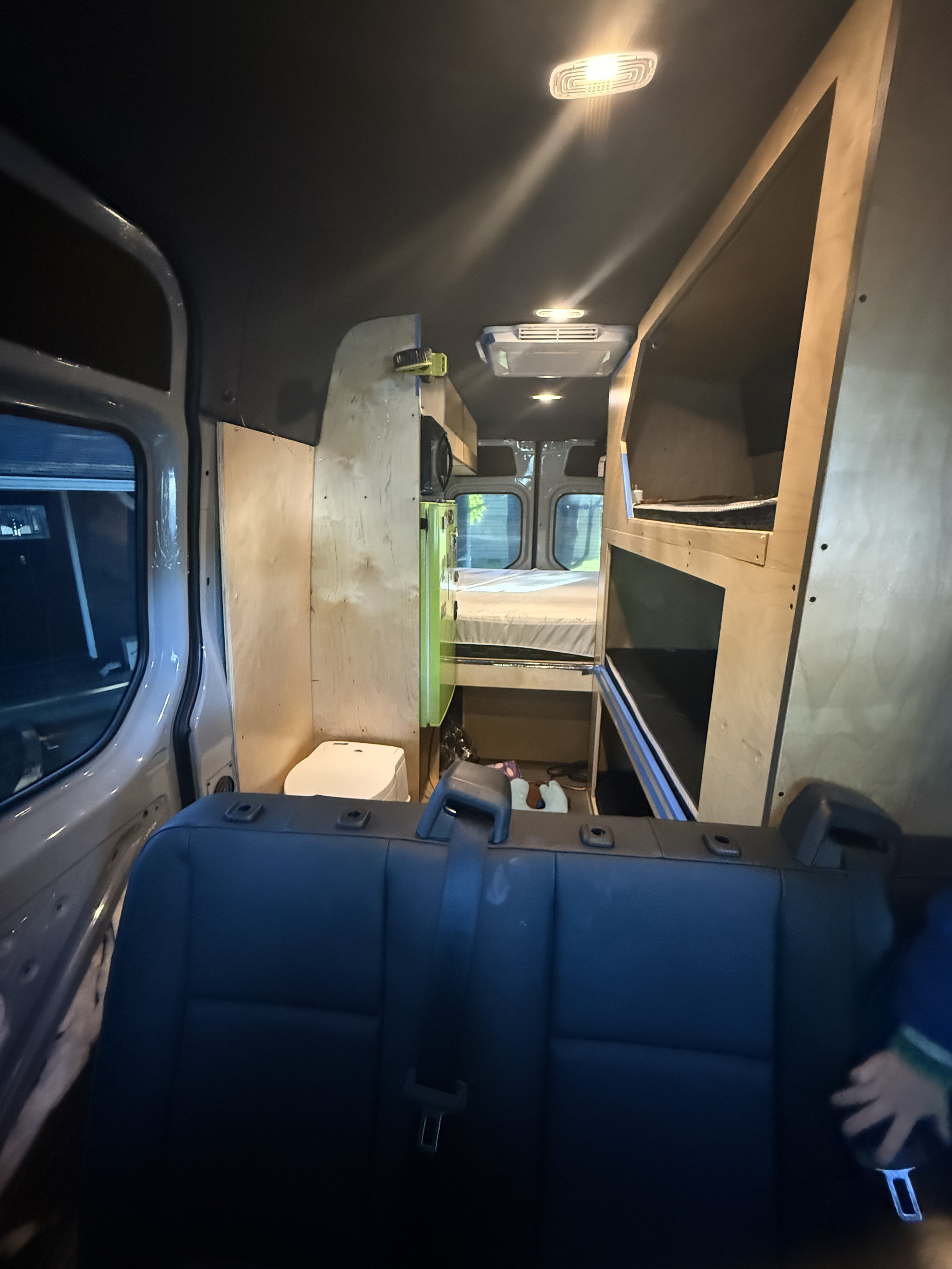 **Custom-built camper van interior featuring a cozy bed, shelving, and a back seat, perfect for your next RV rental adventure.**. Mercedes-Benz Sprinter 2024