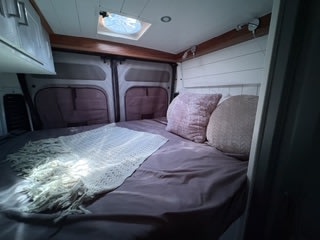 Cozy RV rental bed with plush pillows and blanket in a camper van interior. Perfect for your next van life adventure.. Custom Promaster 2500 2025
