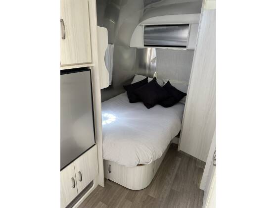 This RV rental's modern bedroom features a compact bed, mini-fridge, and storage cabinets, ideal for cozy road trips.. Airstream Bambi 2021