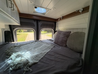 Comfortable RV rental camper van interior. Cozy bed with pillows & a soft throw, offering a scenic view for your next travel adventure.. Custom Promaster 2500 2025