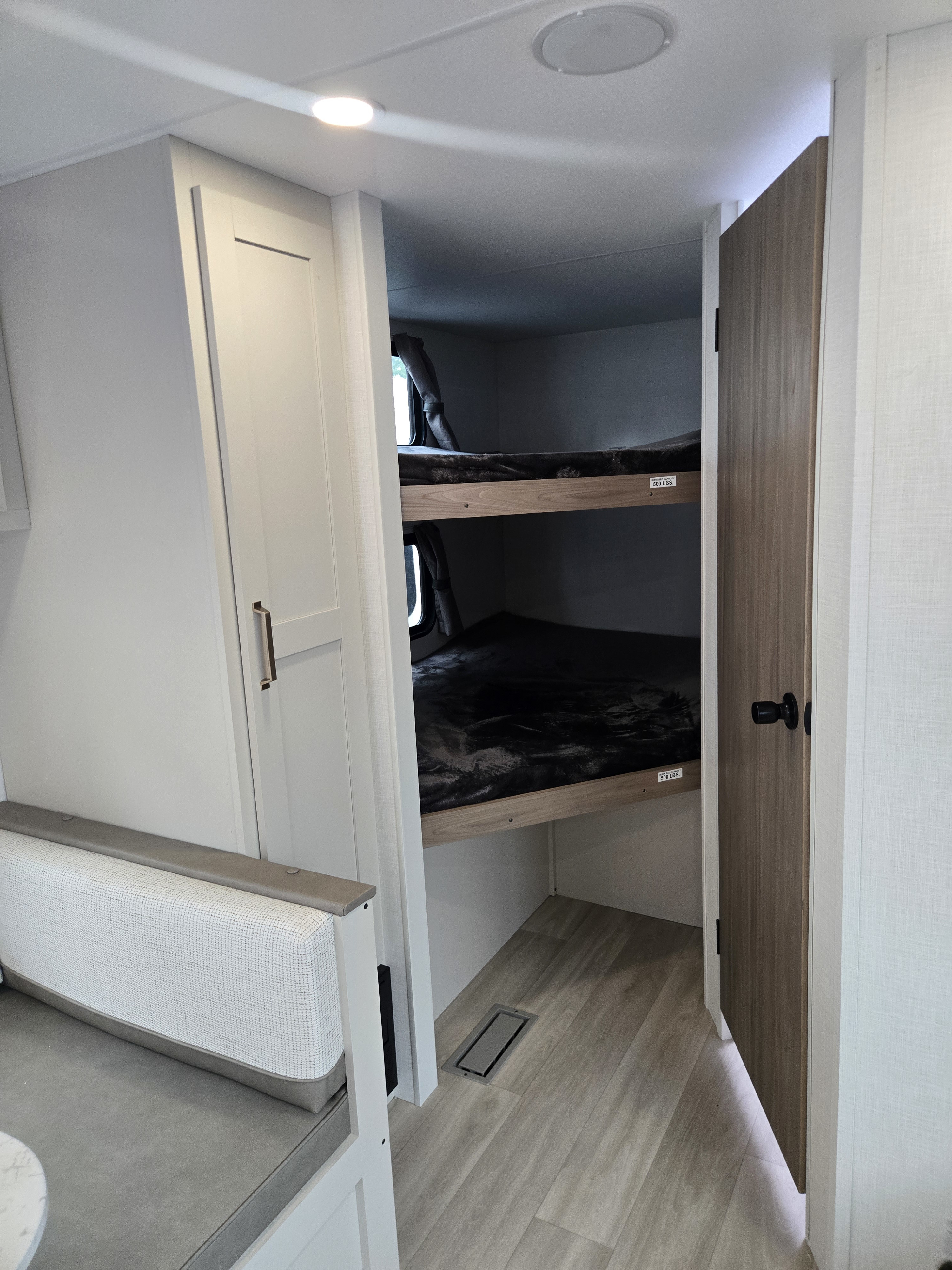 Cozy rv rental interior with bunk beds, dark bedding, cabinet, and open wooden door. Perfect for family adventures.. KZ Sportsmen 291BHK 2027