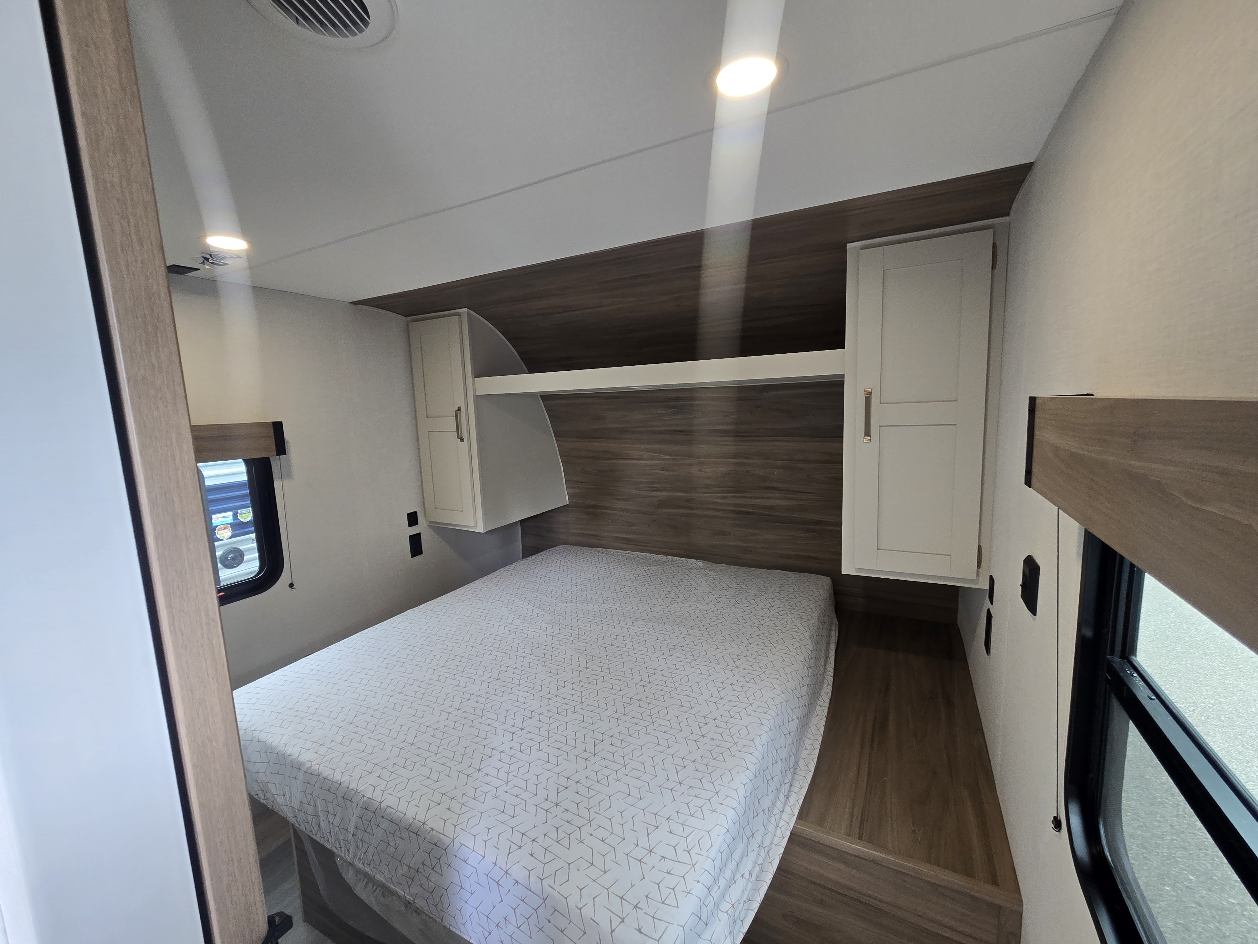 Cozy RV rental bedroom featuring a comfy bed with geometric patterns, overhead cabinets, and soft lighting for travel adventures.. KZ Sportsmen 291BHK 2027
