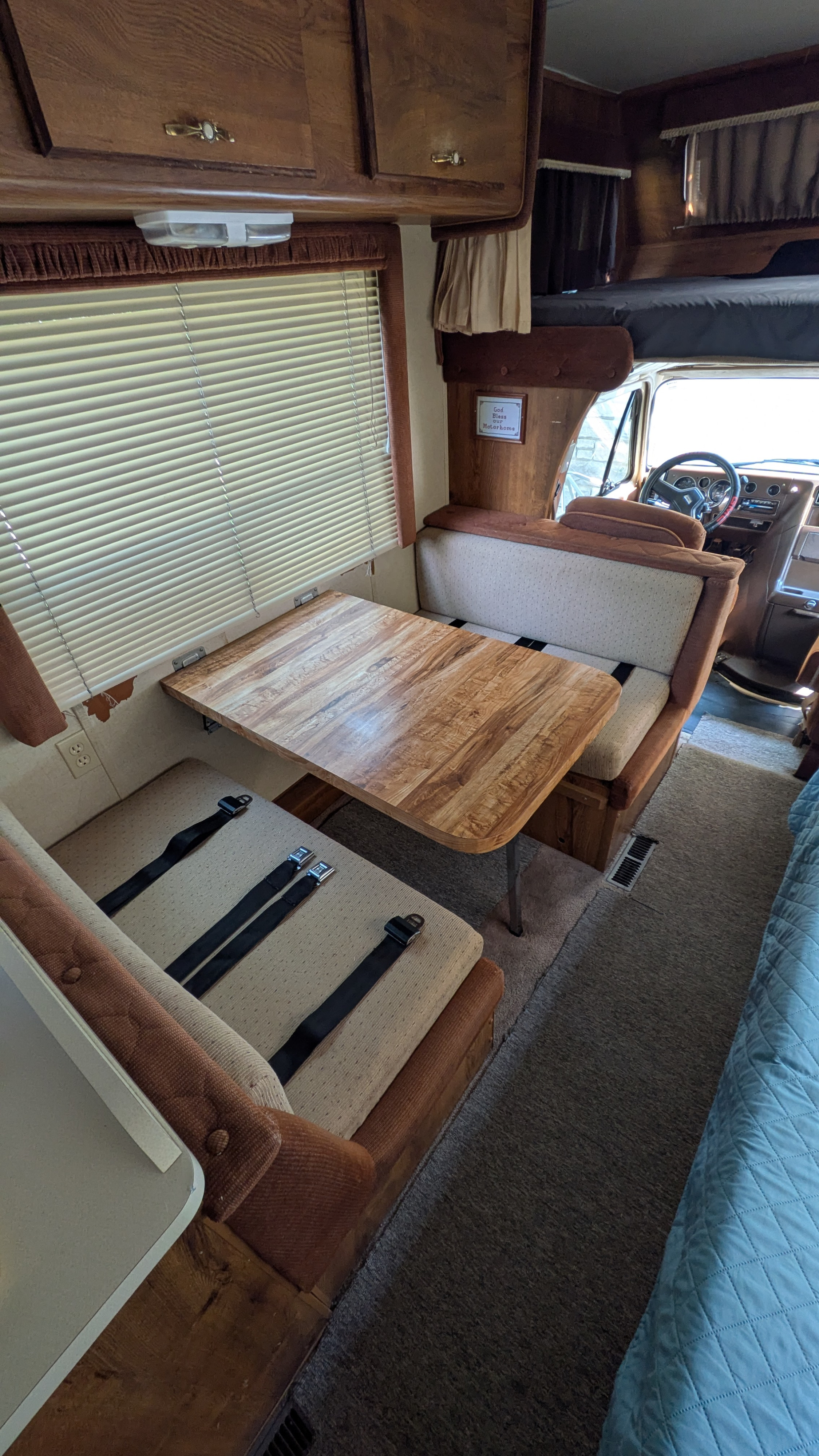 RV rental interior featuring a vintage dinette with a wood table, bench seating, and safety belts. Ideal for road trips.. Gmc Motorhome 1987