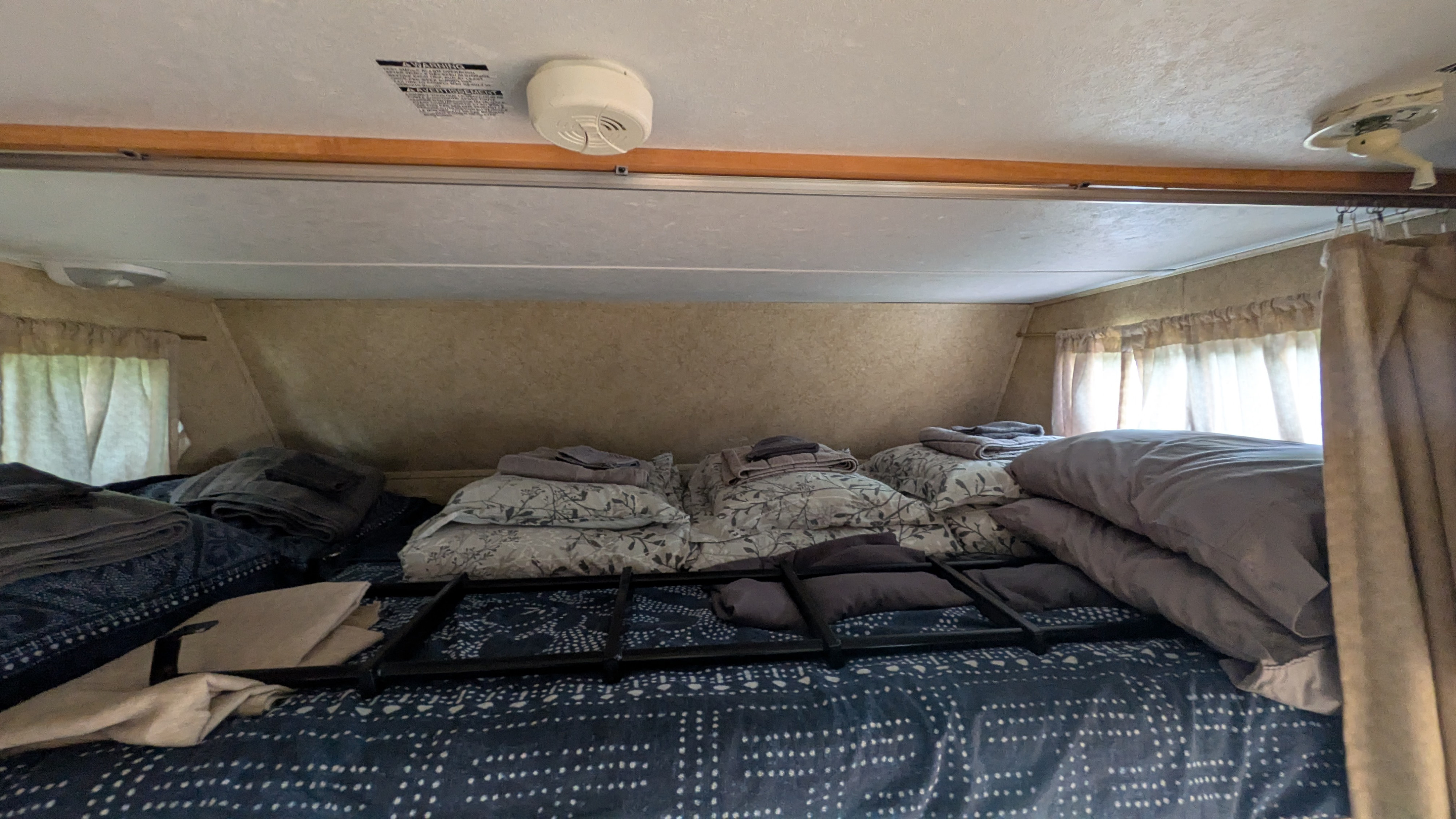 Cozy RV rental sleeping area with bunk bed, pillows, blankets, a smoke detector, and curtains.. Forest River Sunseeker 2010