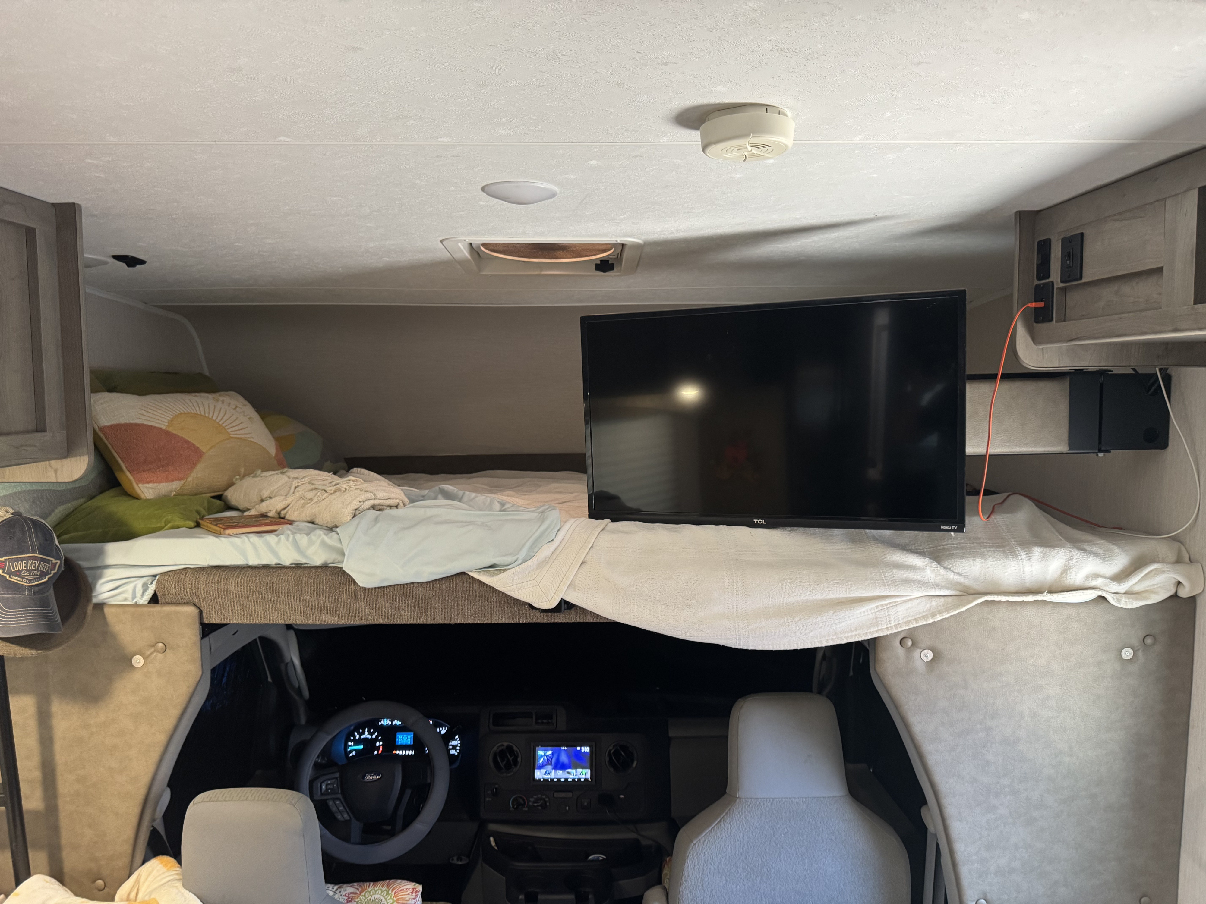 Cozy RV rental interior with an overhead bunk bed and TV above the driver's cab and dashboard. Perfect for travel.. Forest River Coachmen Freelander 2021