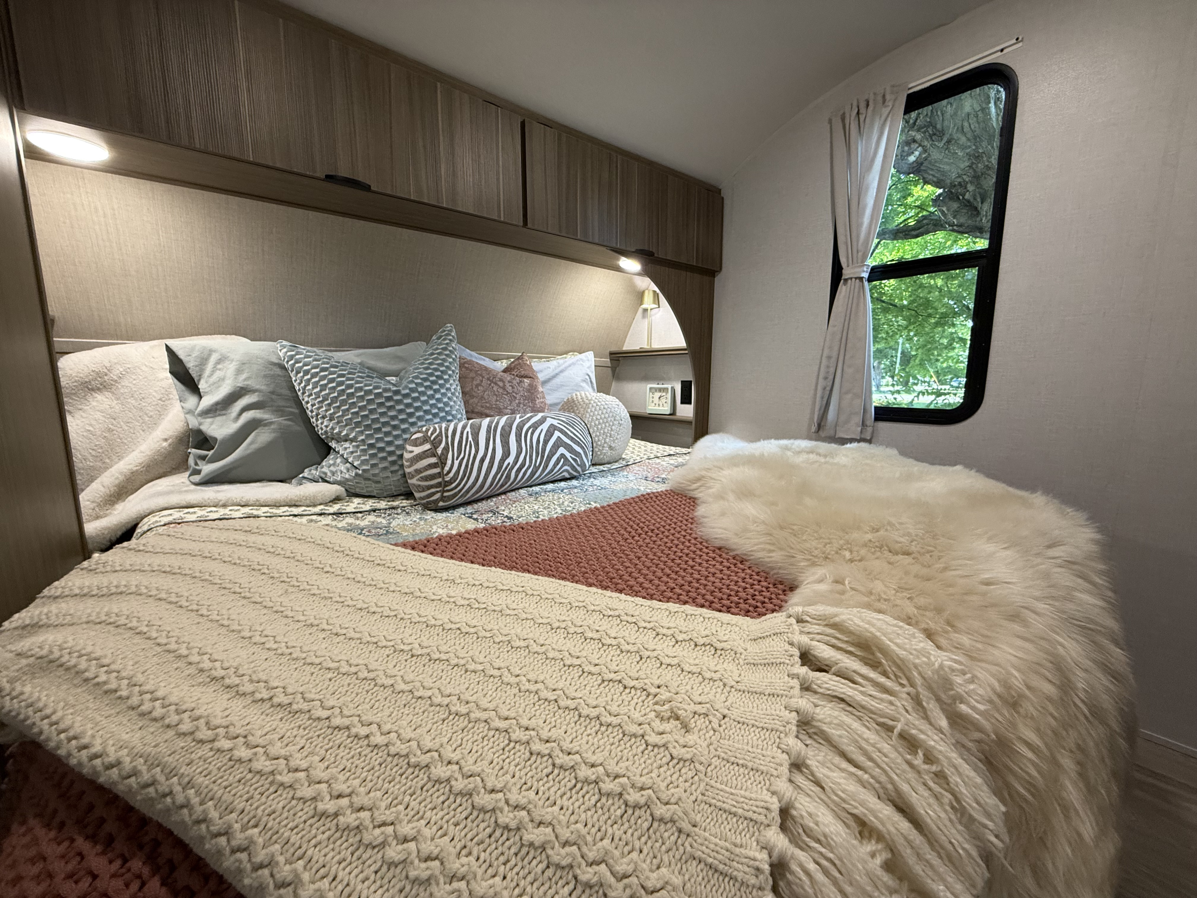 Cozy RV rental bedroom with layered bedding, overhead storage, and a window view. Perfect for comfortable travel.. Forest River Wildwood X-Lite 2026
