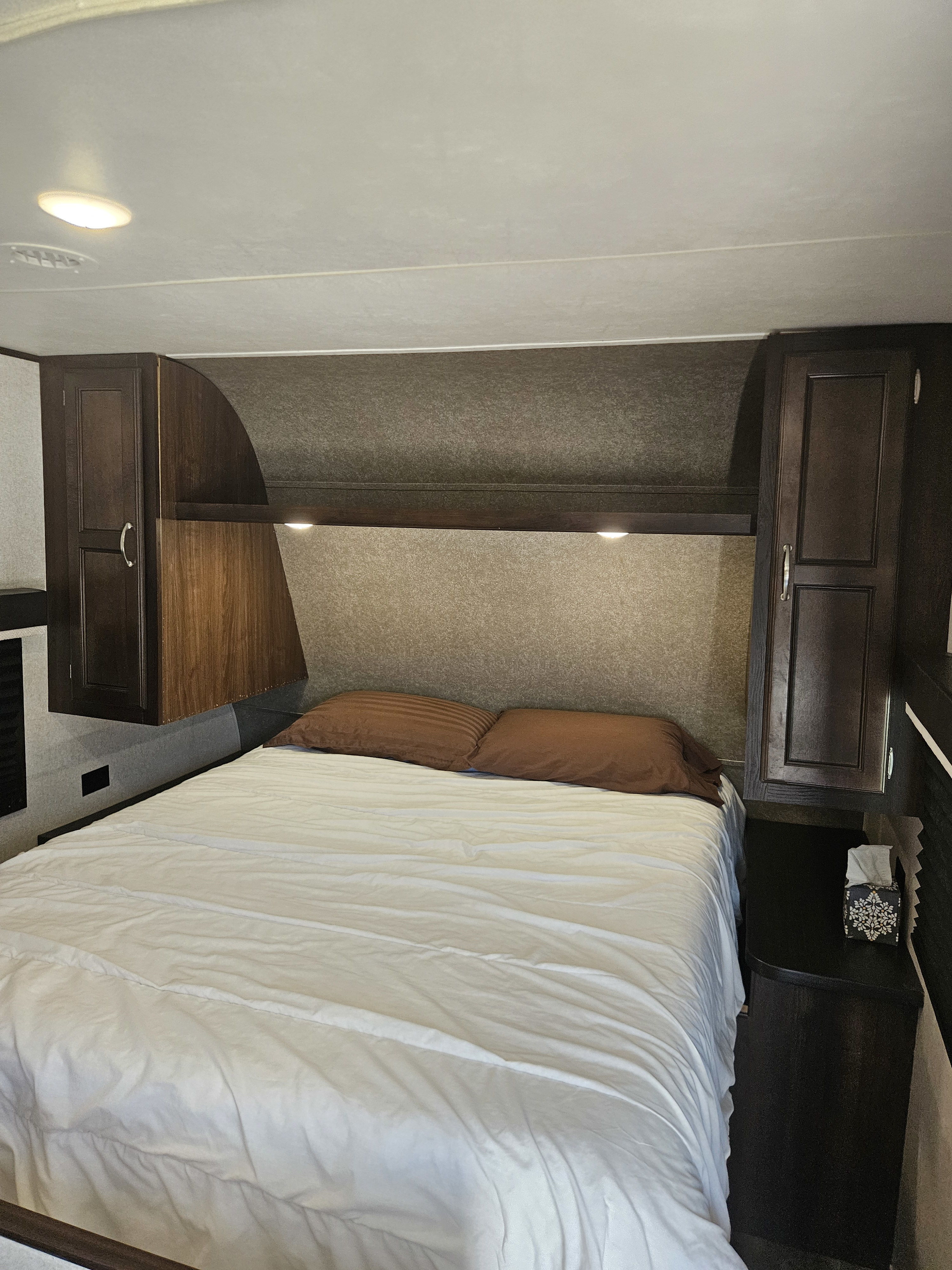 An RV rental bedroom with a neatly made bed, white sheets, brown pillows, and ample dark wood cabinetry.. Jayco Jay Flight SLX Rocky Mountain Edition 2018