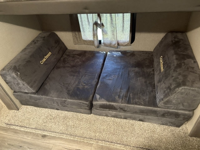 Cozy dark gray modular seating in an RV rental, with "Coachmen" embroidery, carpeted floor, and bunk.. Coachmen Catalina 2022