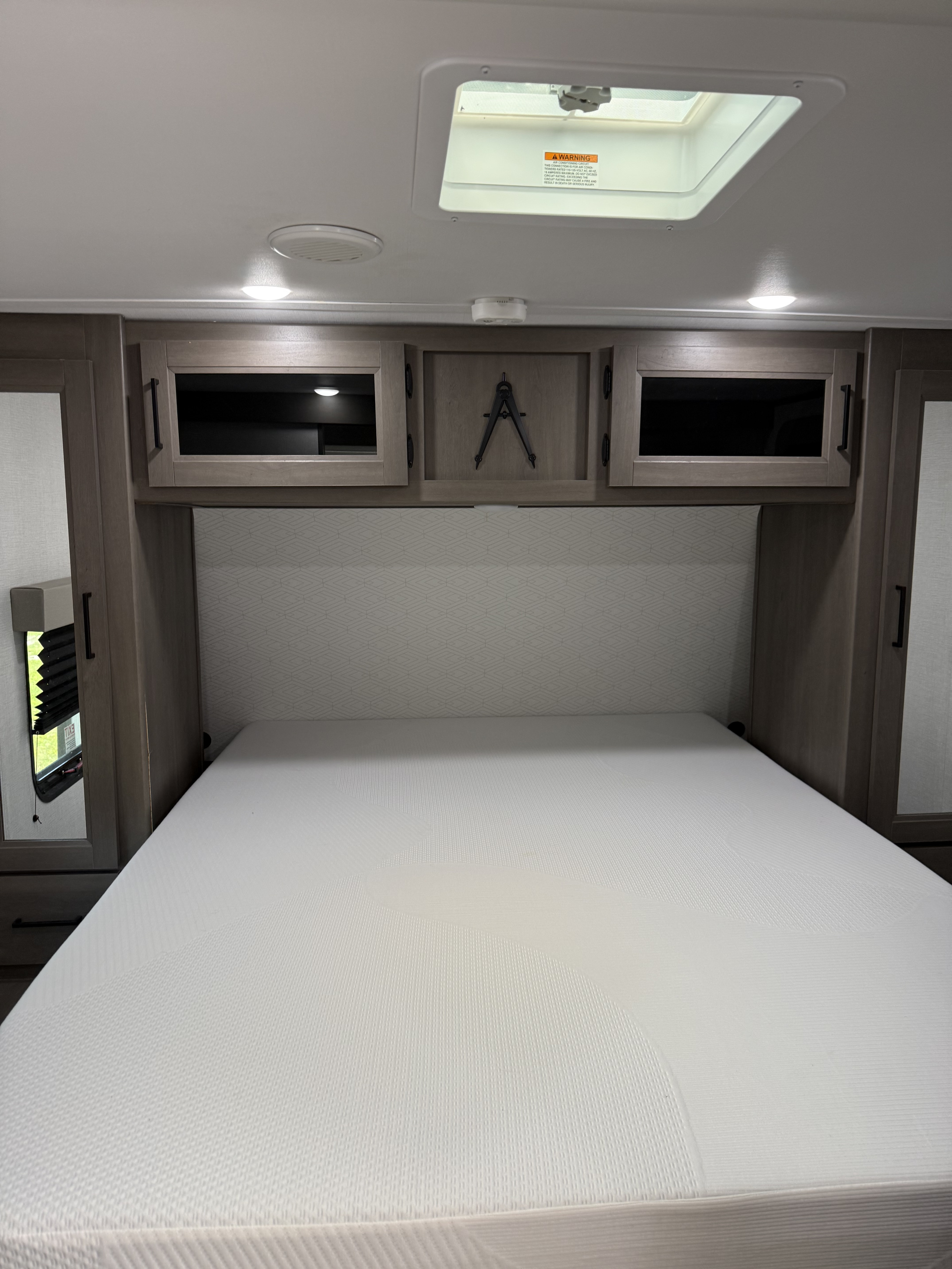 Spacious RV rental bedroom with a comfy mattress, overhead storage cabinets, and a ceiling skylight for natural light.. Grand Design Transcend 2025