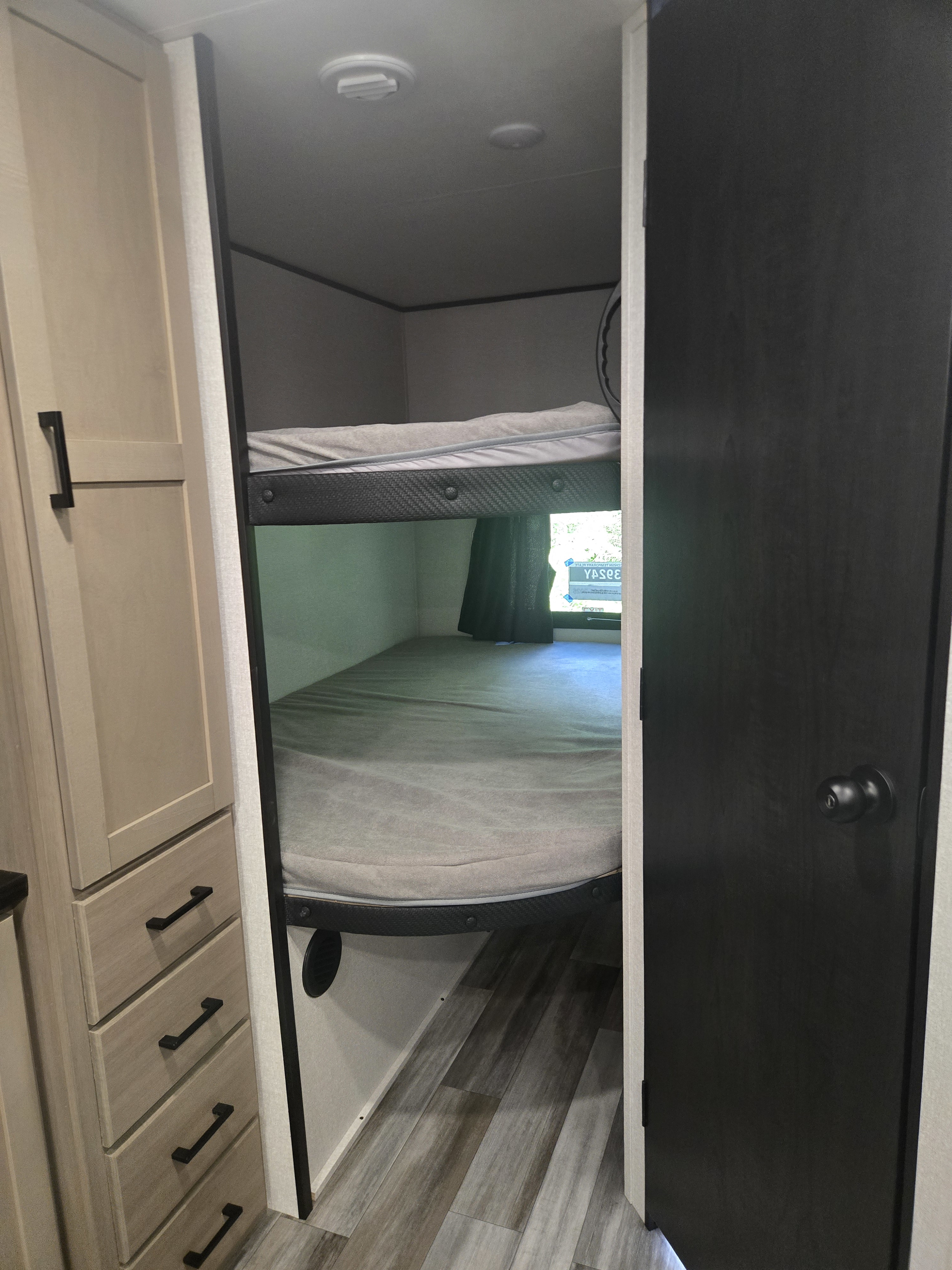 Cozy RV rental interior featuring stacked bunk beds, adjacent light wood cabinets, and a dark bedroom door.. Jayco Jay Flight SLX 2026