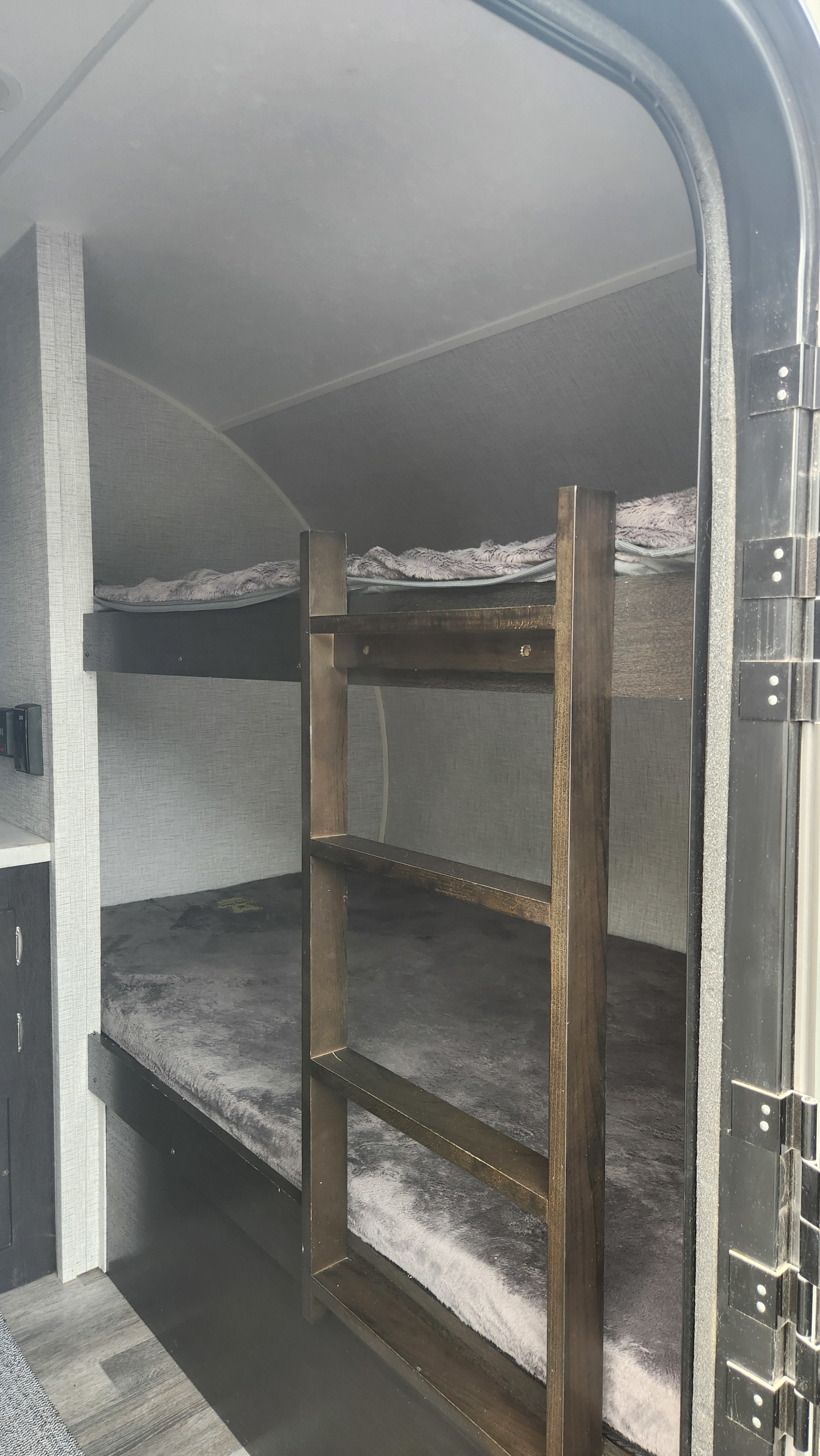 Interior of an RV rental showing stacked bunk beds with soft grey bedding, accessed by a wooden ladder. Cozy and practical.. Braxton Creek Bushwhacker Plus 2021