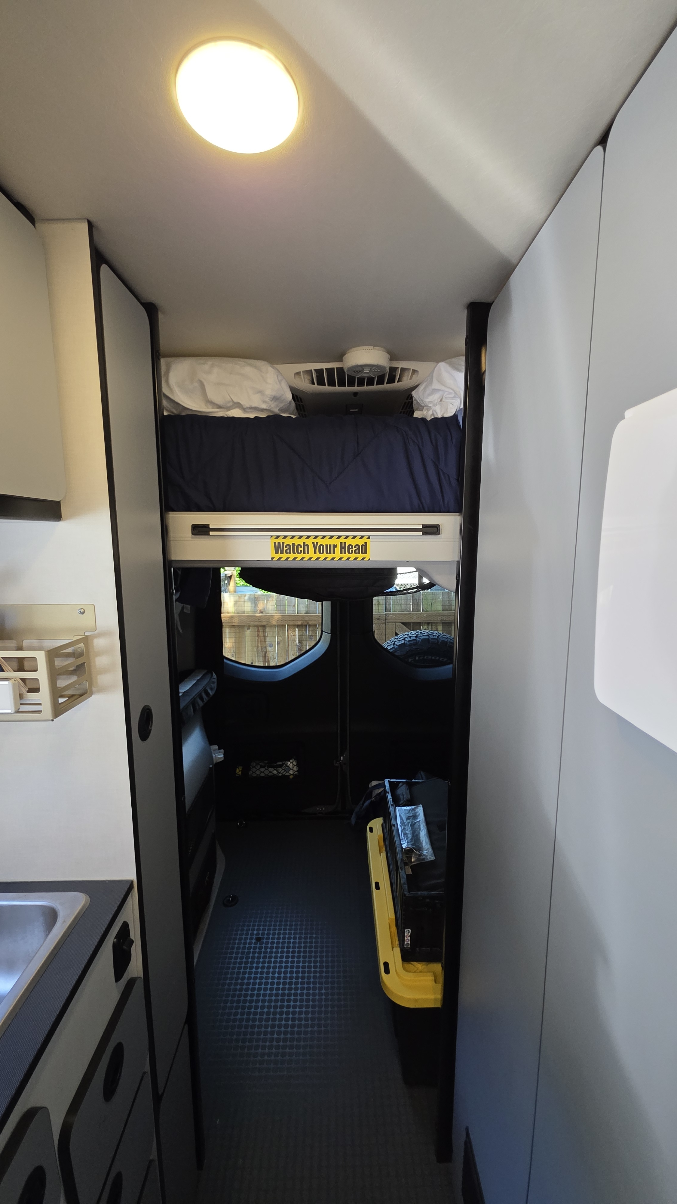 Inside an RV rental: compact campervan interior with suspended bunk bed, kitchen counter, and functional storage space.. Winnebago Revel 2021