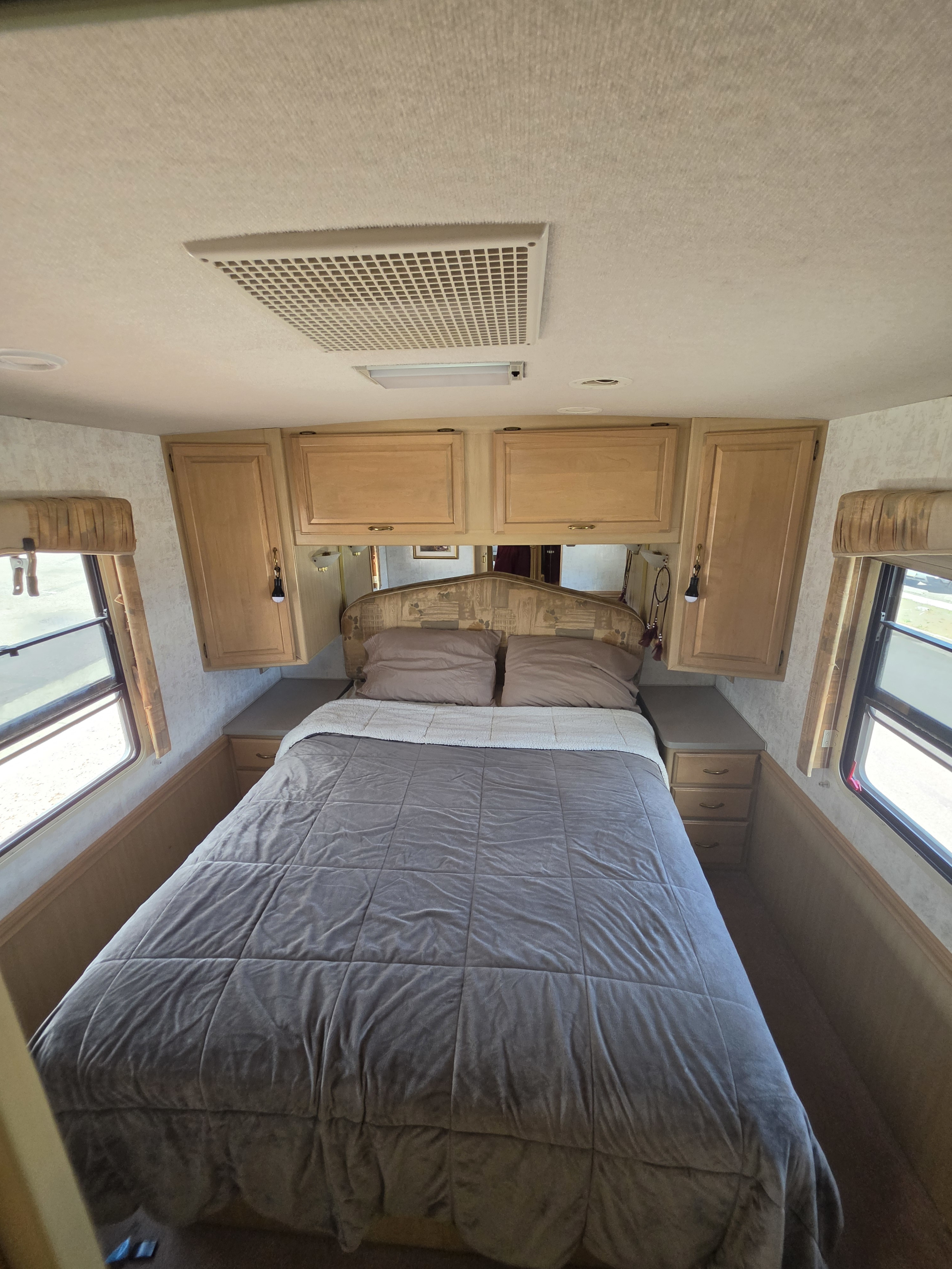Cozy RV rental bedroom with a comfortable bed, built-in cabinets, and windows on both sides.. Winnebago Itasca Sunova 1998