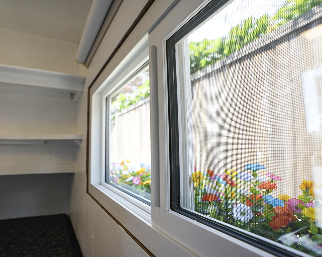 RV rental interior: A screened window offers colorful flower views. Shelves line the compact, cozy space.. Micro-Lite Micro Camper 1987