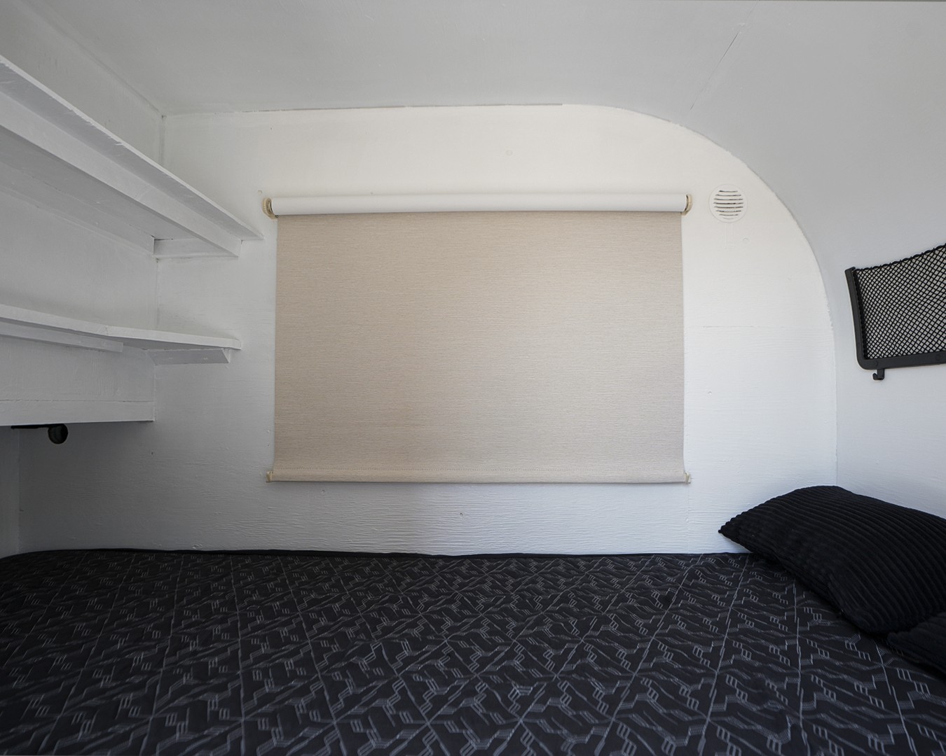 Cozy RV rental sleeping area featuring a dark patterned bed, pull-down blind, built-in shelves, and wall vent.. Micro-Lite Micro Camper 1987