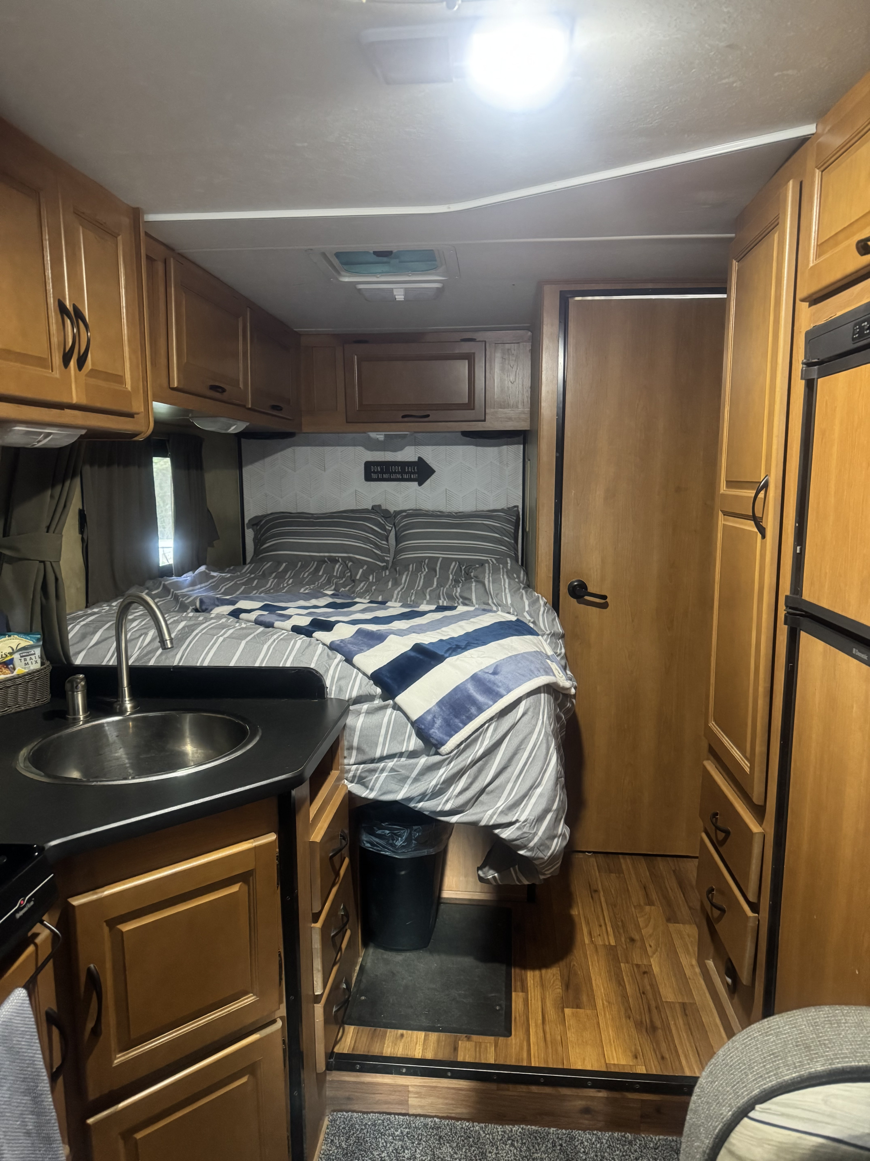 This cozy rv rental interior features a bed with striped bedding, a small kitchen sink, and warm wood cabinetry.. Thor Majestic 2013