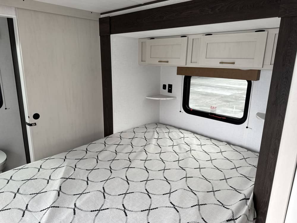 Cozy RV rental bedroom featuring a bed with modern white and dark wood decor, overhead storage, and a window.. Crossroads RV Zinger 2026