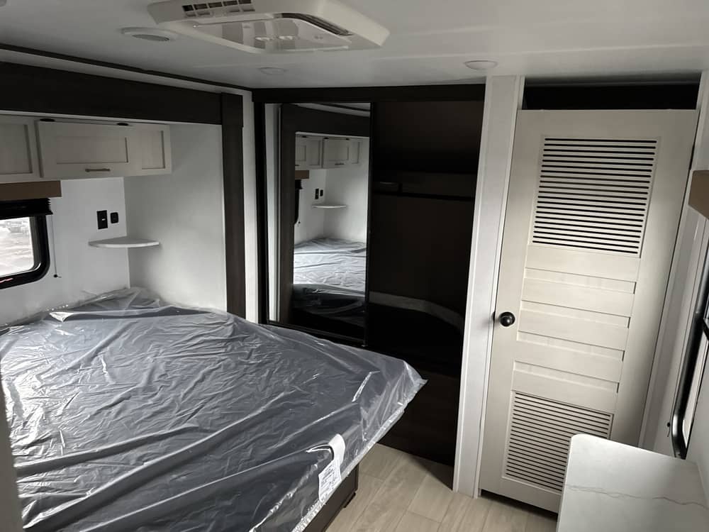 Cozy RV rental bedroom with a fresh bed, overhead cabinets, and compact storage solutions for your adventures.. Crossroads RV Zinger 2026
