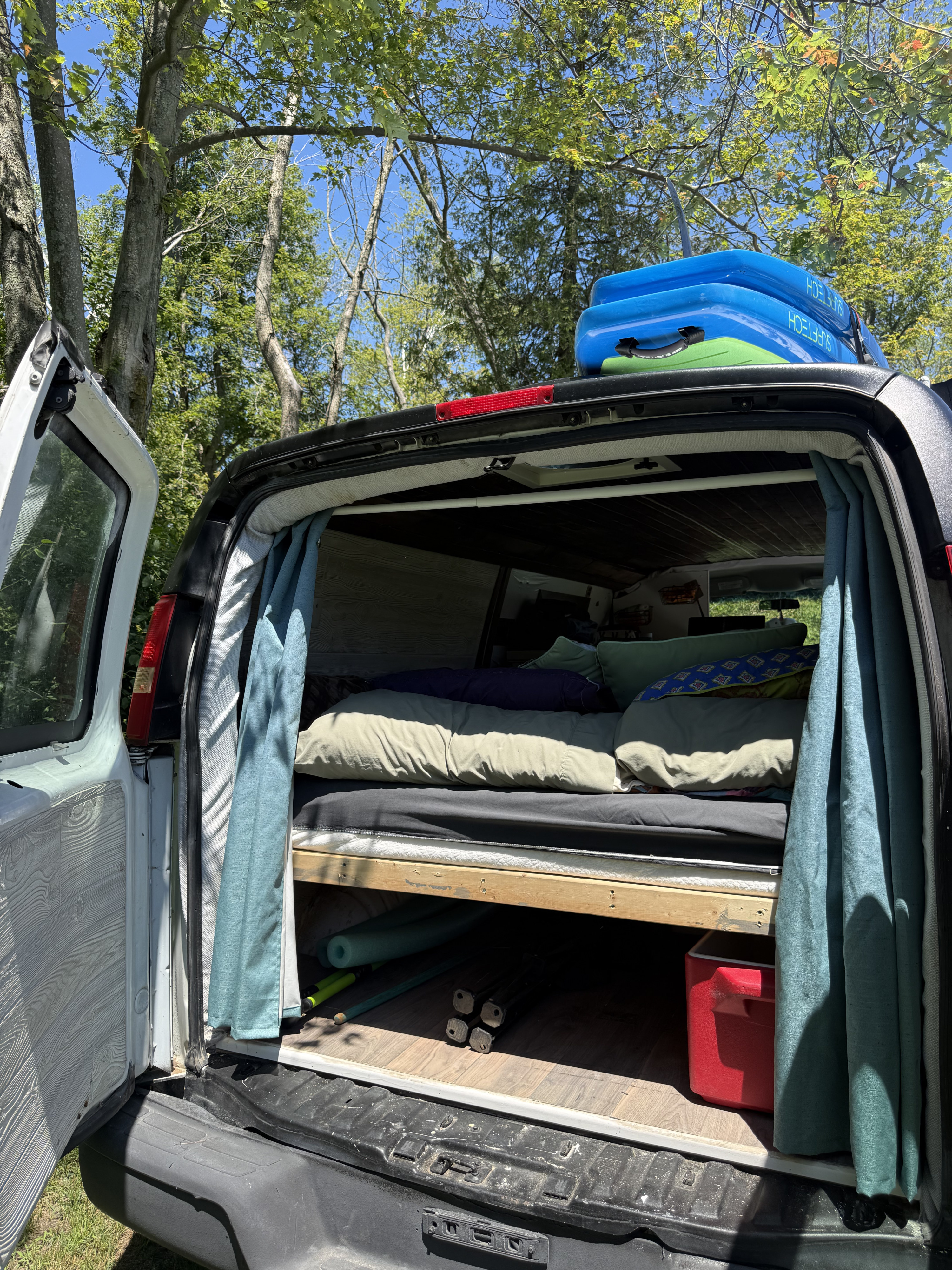 Custom camper van interior with bed, storage, and paddleboards on the roof, showing an ideal setup for an rv rental.. Chevrolet express 2007