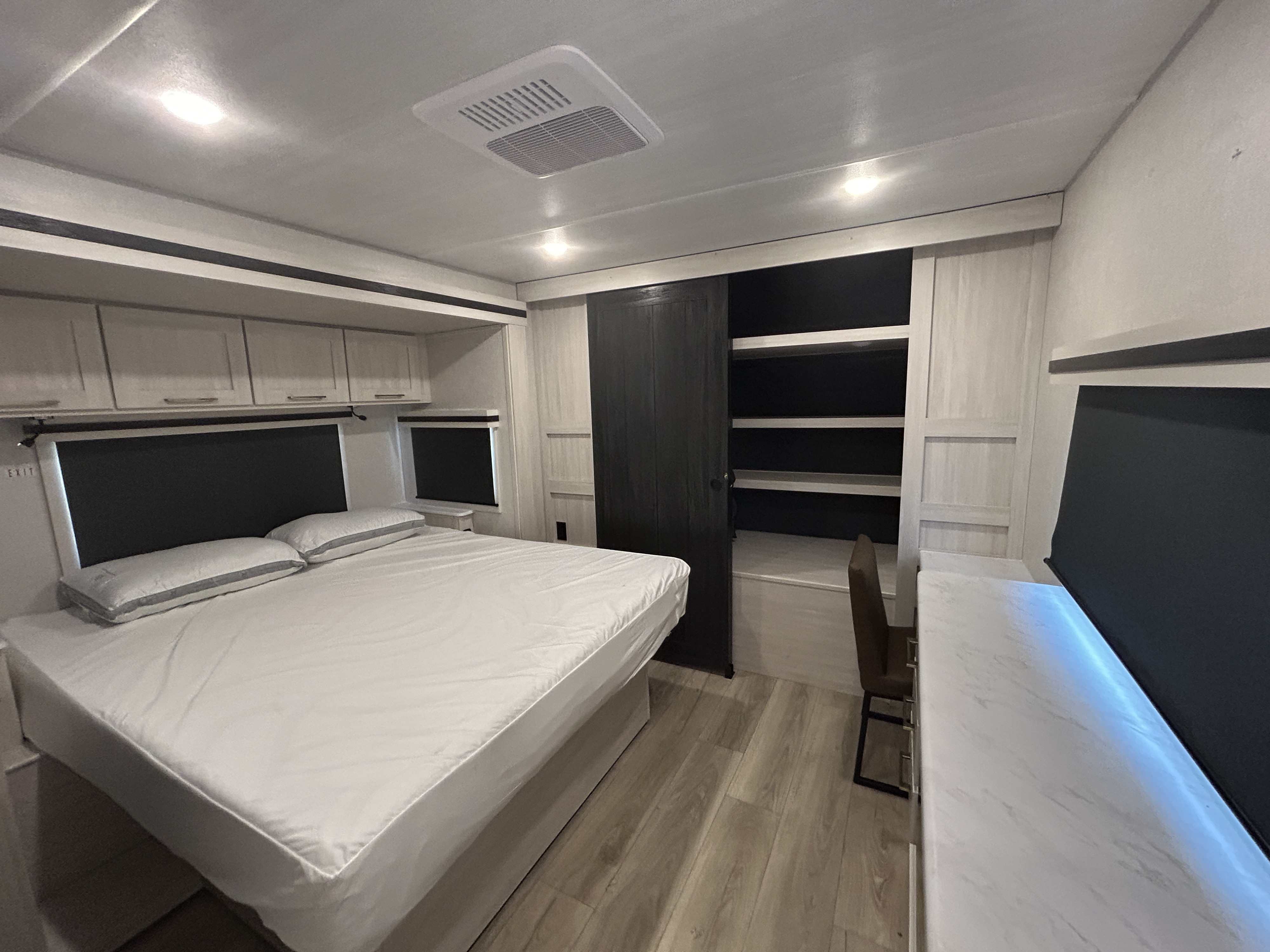 Modern rv rental bedroom with a comfortable bed, overhead cabinets, closet, and a small desk for a complete setup.. Forest River Grand Surveyor 2025