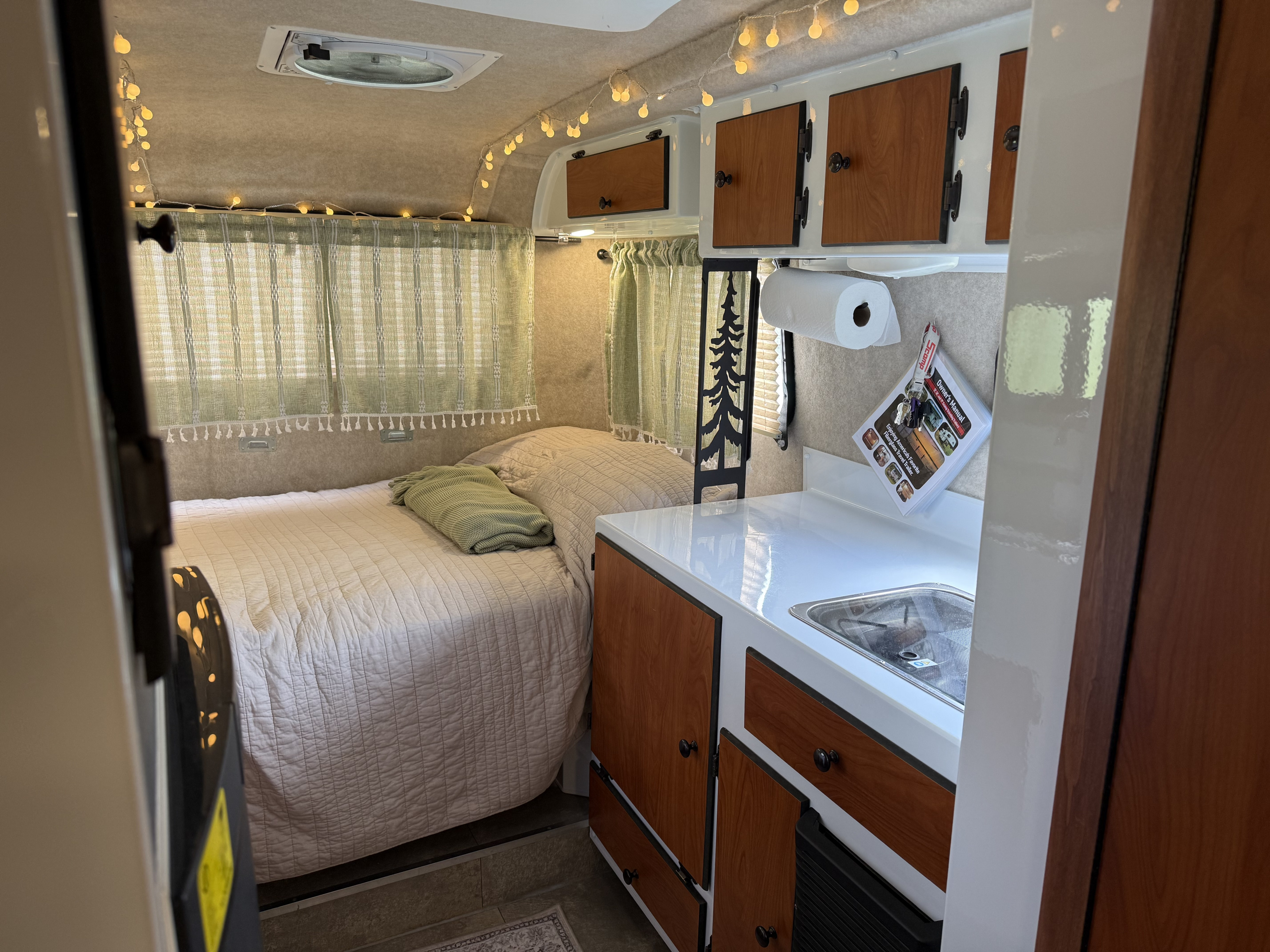 Inside a cozy rv rental: features a comfy bed, small kitchen with a sink, cabinets, and charming string lights overhead.. Scamp Scamp Trailer 2022