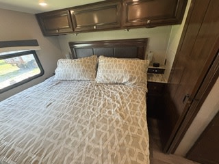 Comfortable RV rental bedroom featuring a large bed with patterned bedding, overhead cabinets, and a window for scenic views.. Fleetwood FLAIR 2020