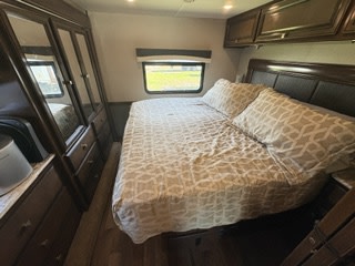 Comfortable RV rental bedroom: large bed with patterned bedding, window, and dark wood wardrobe/drawers.. Fleetwood FLAIR 2020
