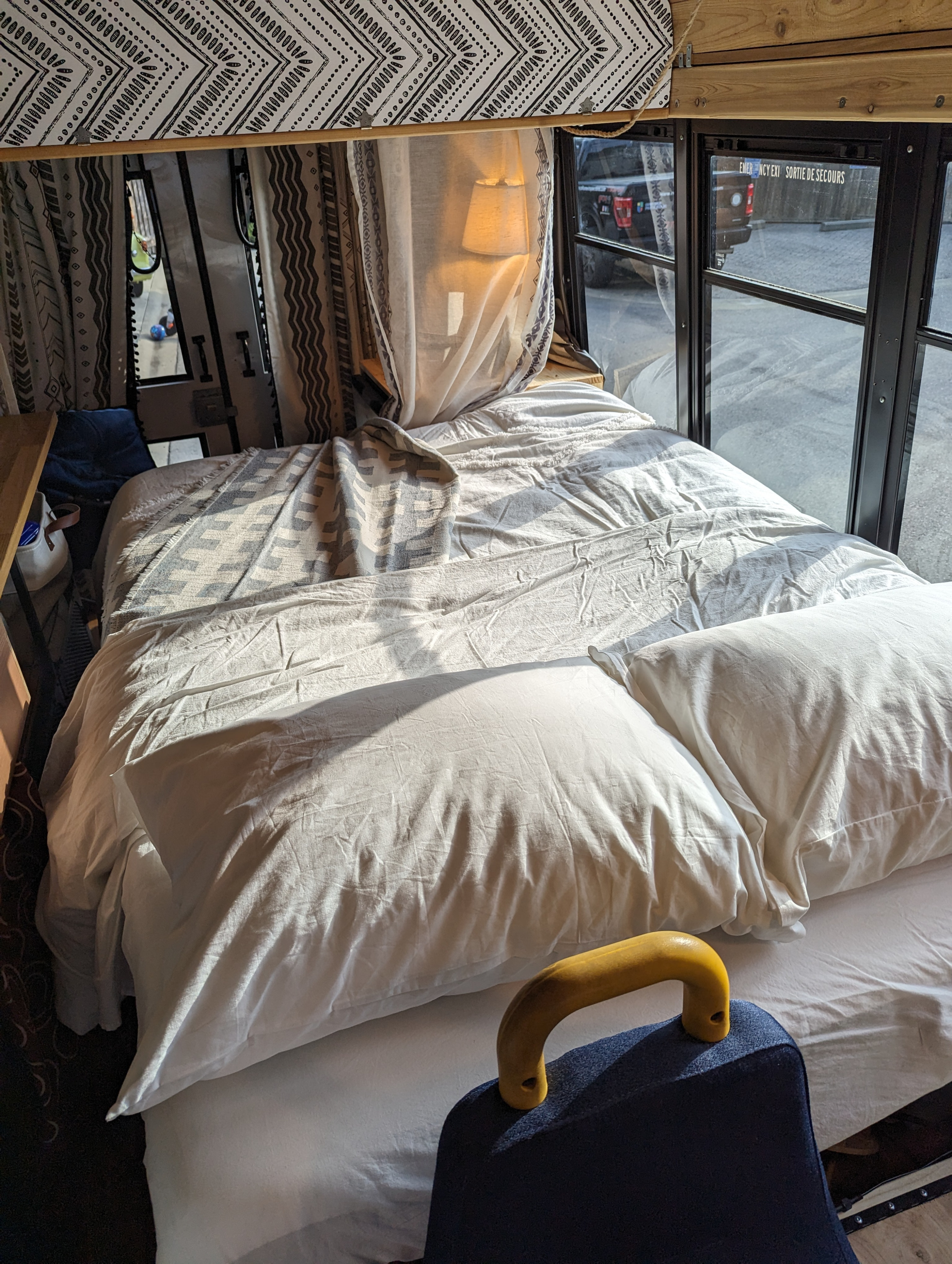 Cozy RV rental bedroom: a large bed with white linens and patterned throw, sunlight streaming through adjacent windows.. Chevrolet Express 2011