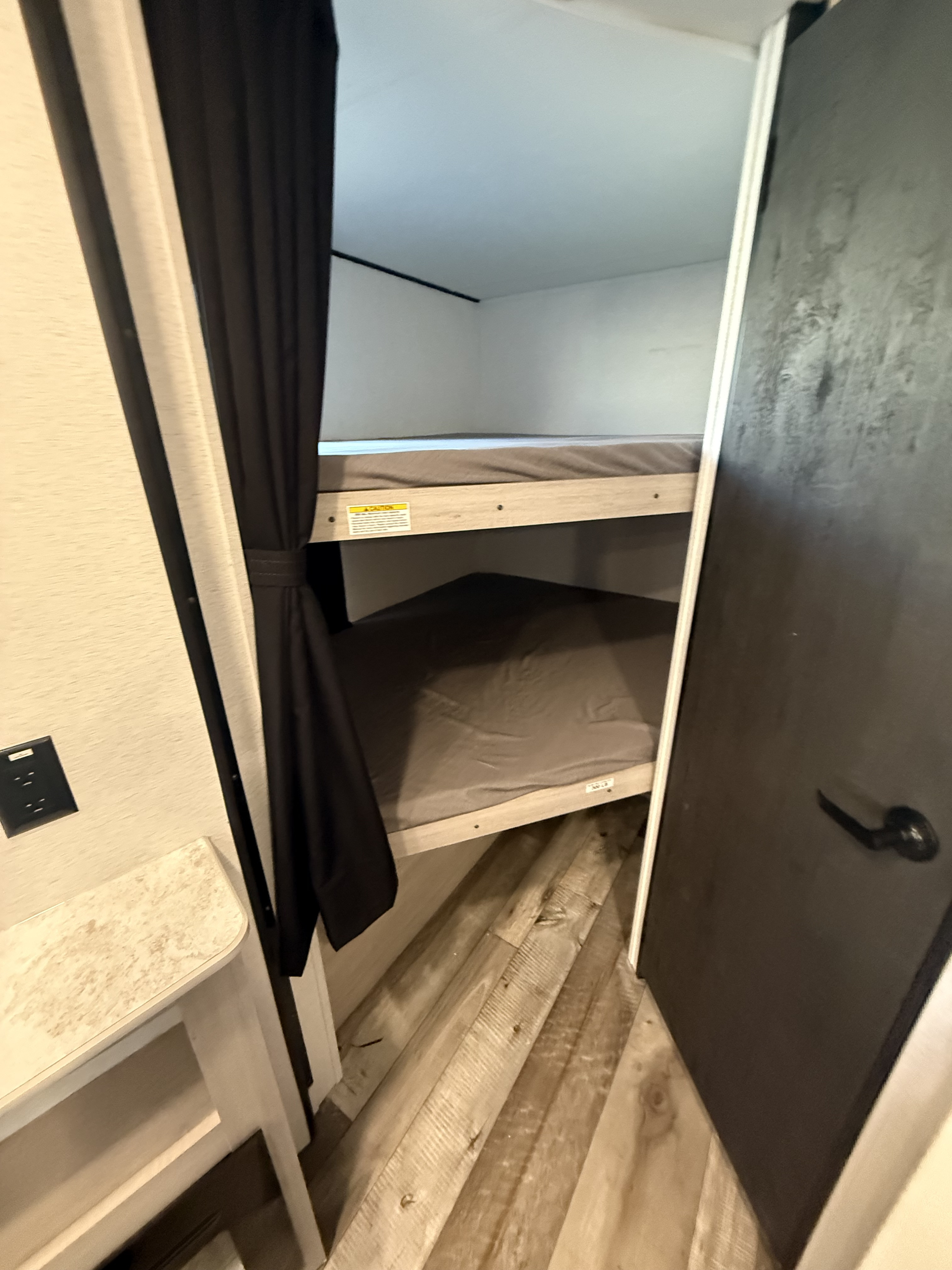 Cozy bunk beds in an **rv rental**, featuring dark privacy curtains and wood-look flooring. Ideal for family adventures.. Crossroads RV Sunset Trail Sport 2025