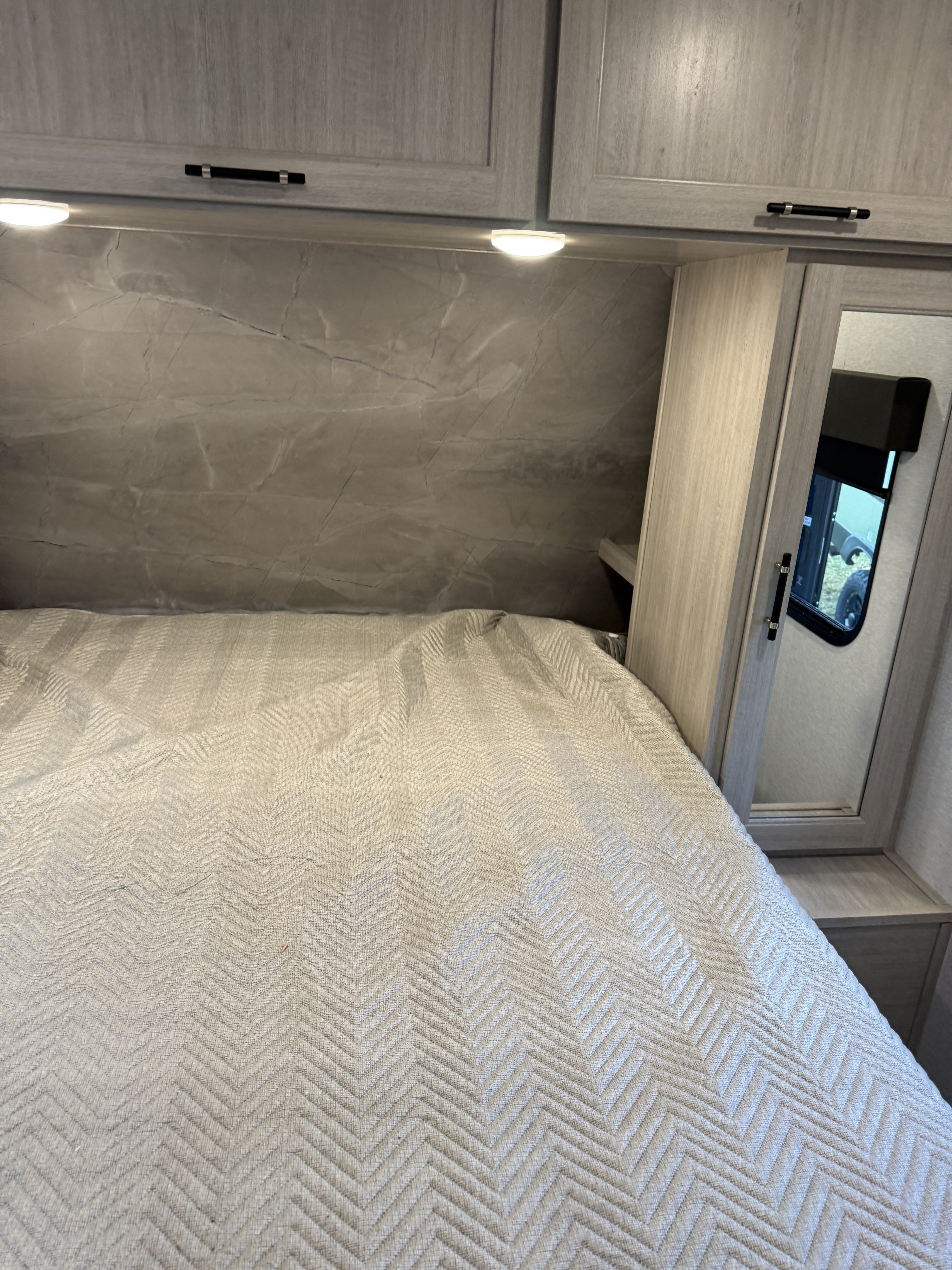 RV rental bedroom with light wood grain cabinets, under-cabinet lighting, marbled headboard, and a chevron-patterned bed.. Crossroads RV Sunset Trail Sport 2025