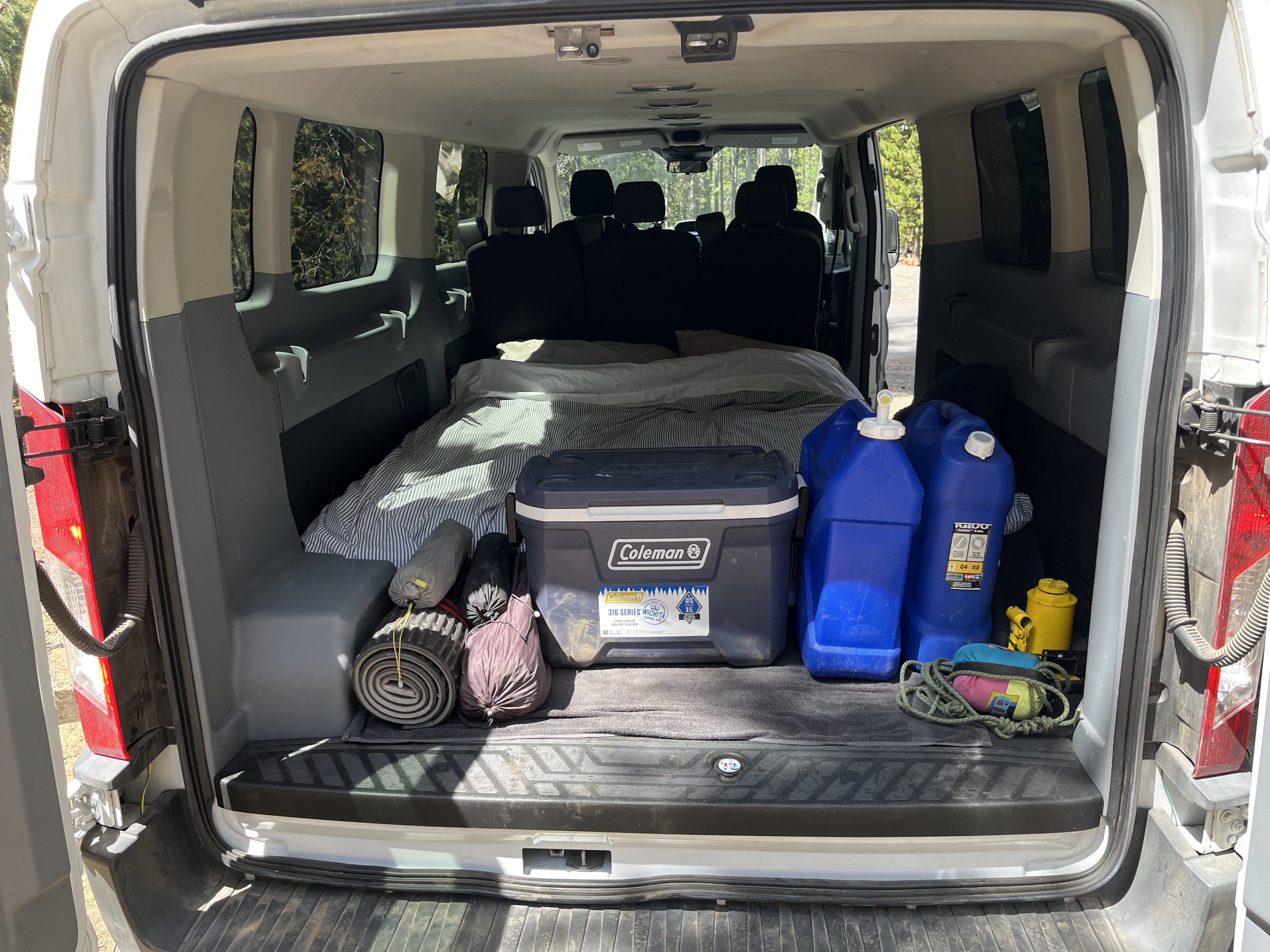 RV rental van's back packed with a bed, Coleman cooler, water jugs, and camping gear for an outdoor adventure.. ford transit 2017