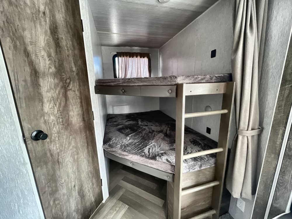 This RV rental features comfortable bunk beds with a ladder, perfect for family sleeping. A cozy sleeping area within the camper.. Forest River Wildwood 2022